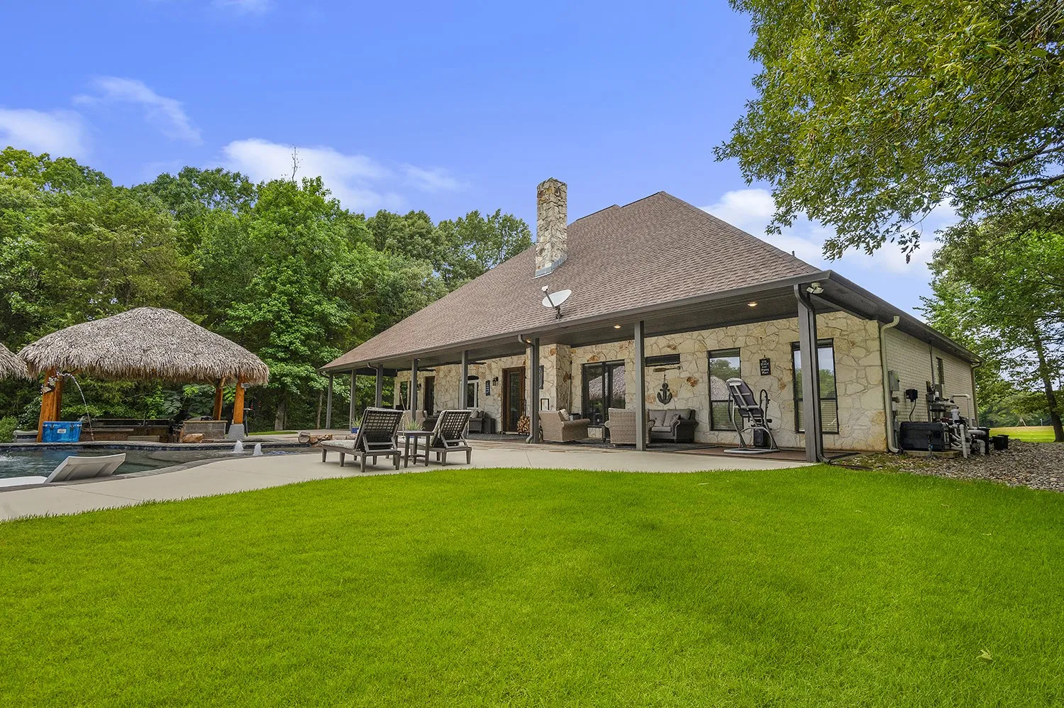 Expansive backyard featuring a stone-clad exterior, covered patio, outdoor pool, and a thatched-roof cabana