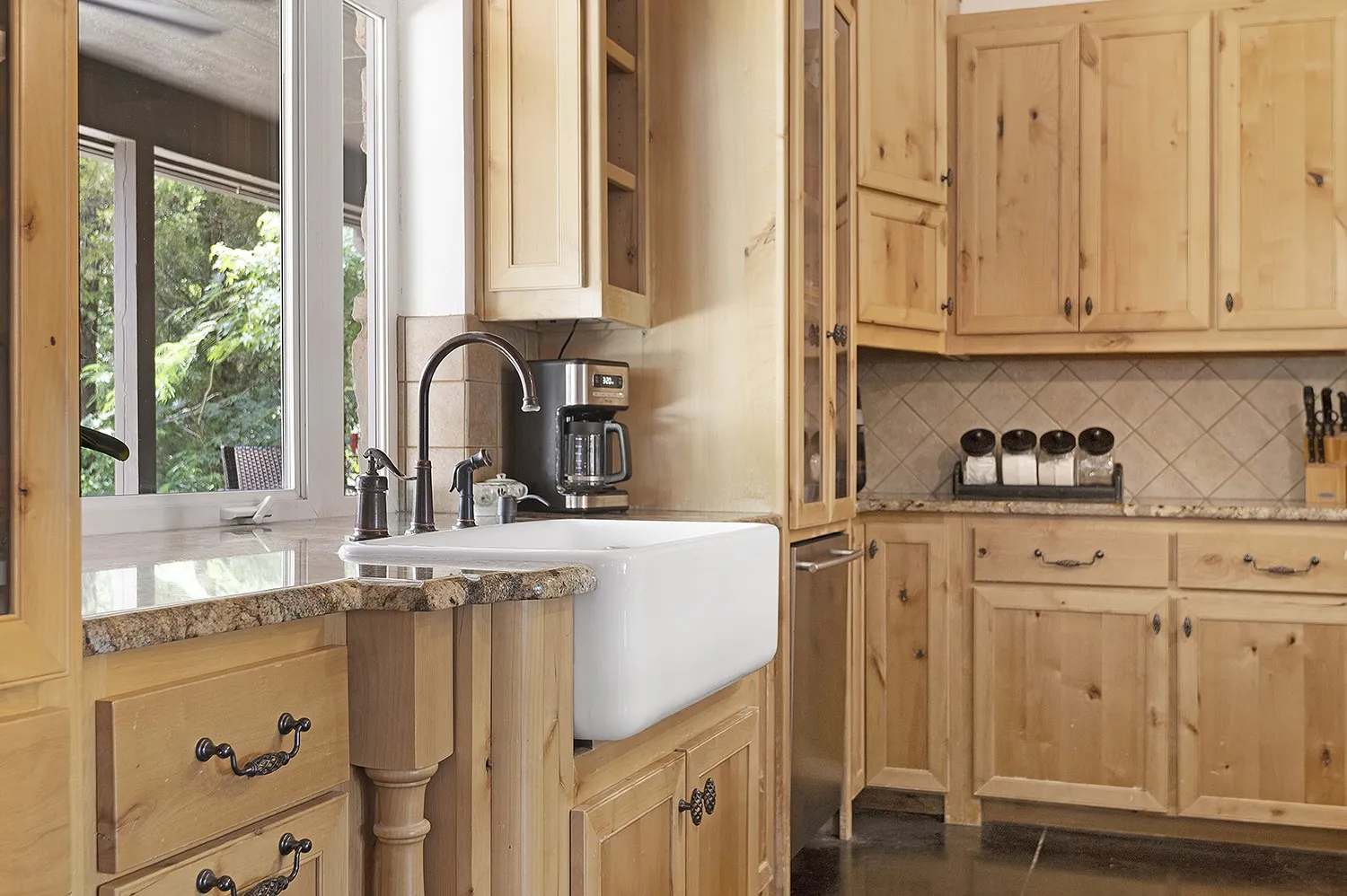 Kitchen featuring light wood cabinetry, granite countertops, a farmhouse sink with a dark bronze faucet, a tiled backsplash, and stainless steel appliances