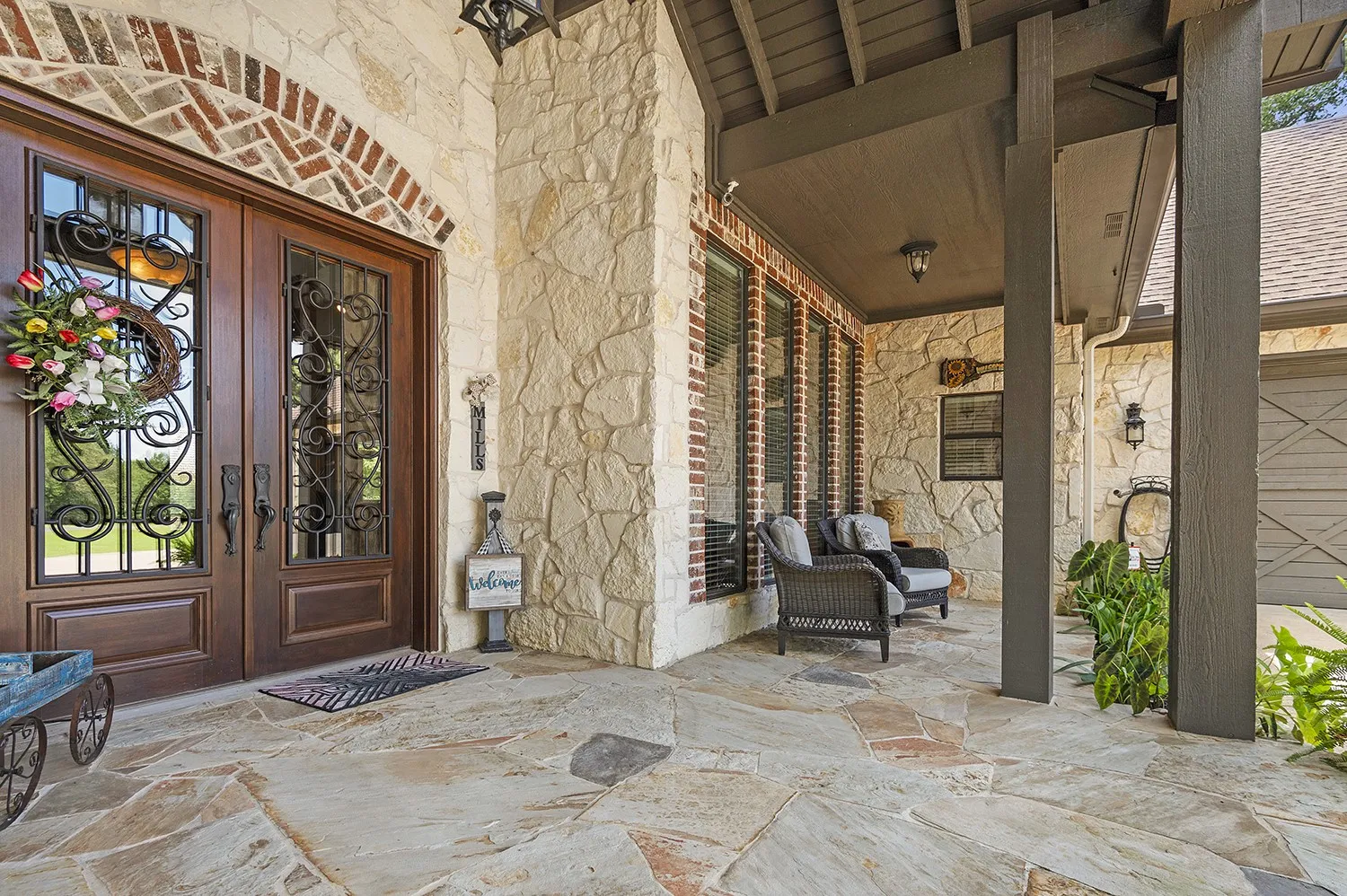 Covered front porch featuring flagstone flooring, stone facade, brick accents, and a double entry door with decorative ironwork