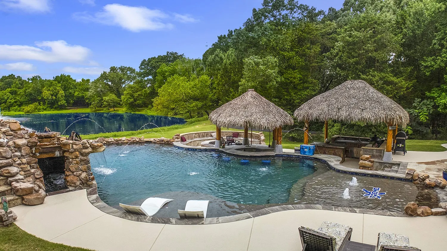 Custom-shaped pool featuring a rock waterfall, integrated spa, swim-up bar with seating, two thatched cabanas, and ample surrounding patio space