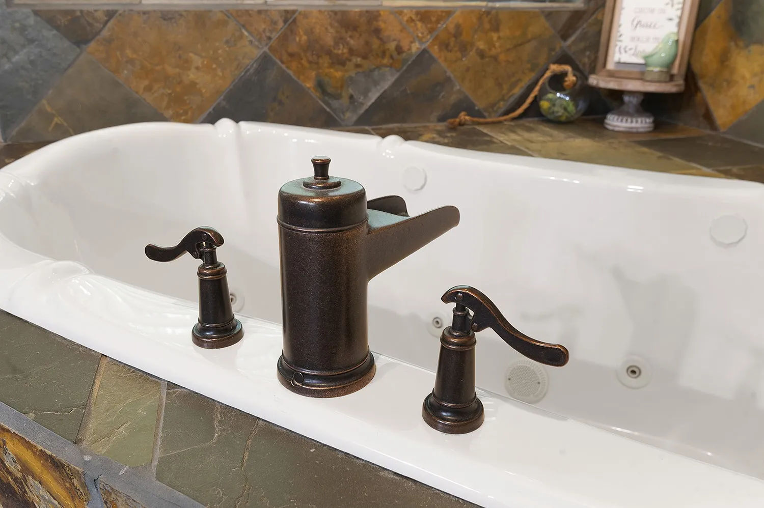Jetted soaking tub with an oil-rubbed bronze faucet set and natural stone tile surround