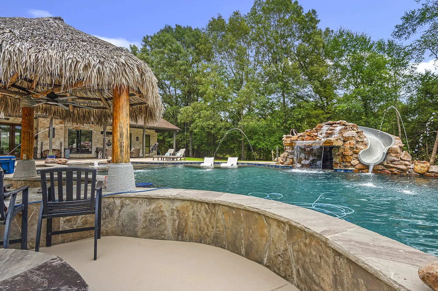 Expansive outdoor oasis featuring a large swimming pool with a rock waterfall, integrated water slide, and multiple water features
