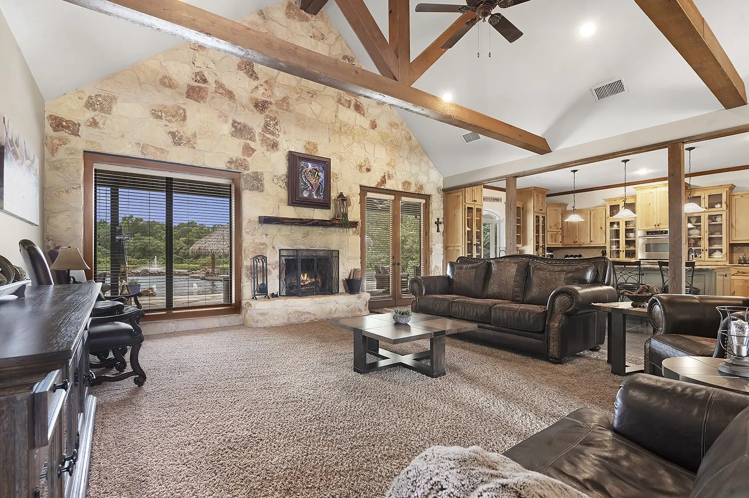 Spacious living area featuring a stone accent wall with a fireplace, vaulted ceiling with exposed wood beams, and a ceiling fan