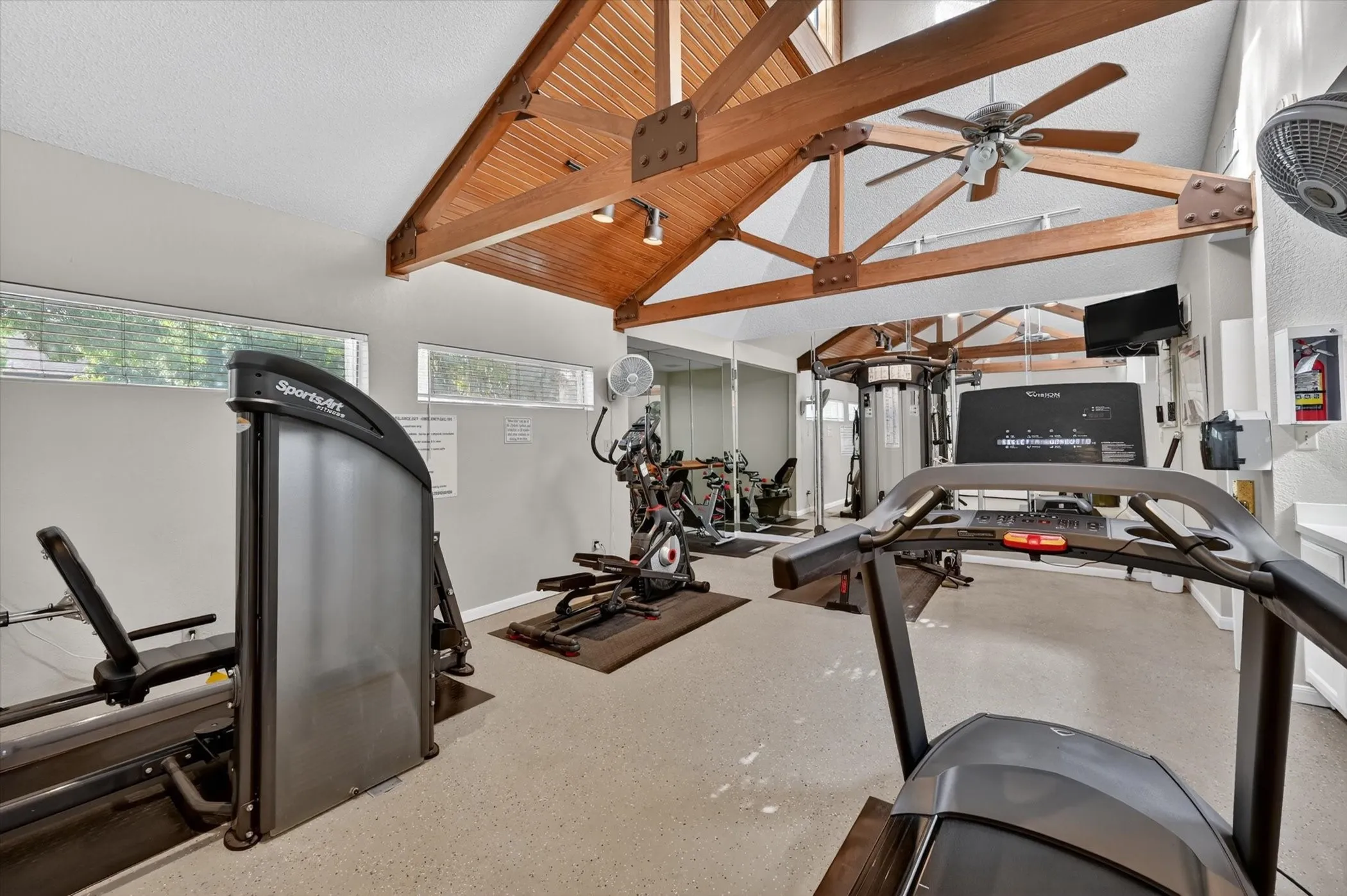 Fitness room featuring a vaulted ceiling with exposed wood beams, track lighting, and a ceiling fan