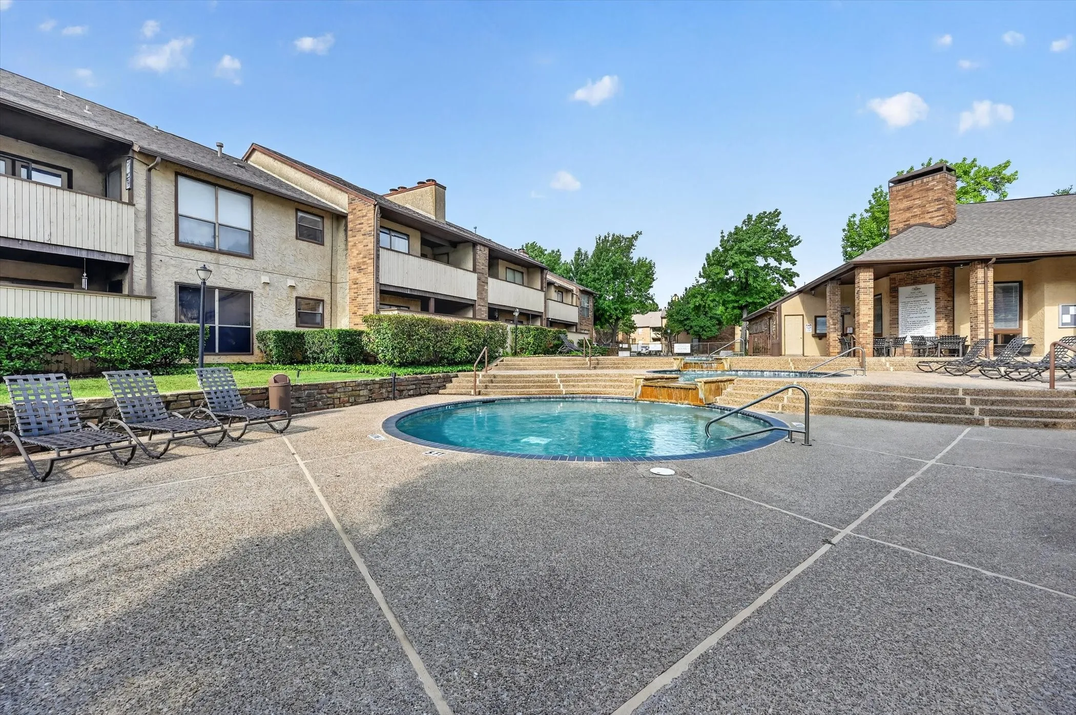 Circular pool with an integrated spa, surrounded by a textured concrete deck and tiered hardscaping