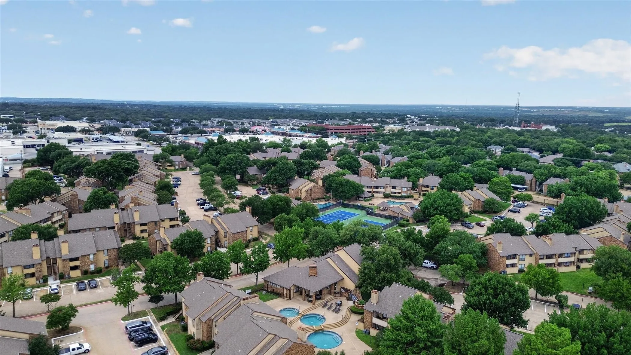Aerial perspective showcasing a multi-building residential community featuring mature trees, surface parking, and a community pool area with multiple spas