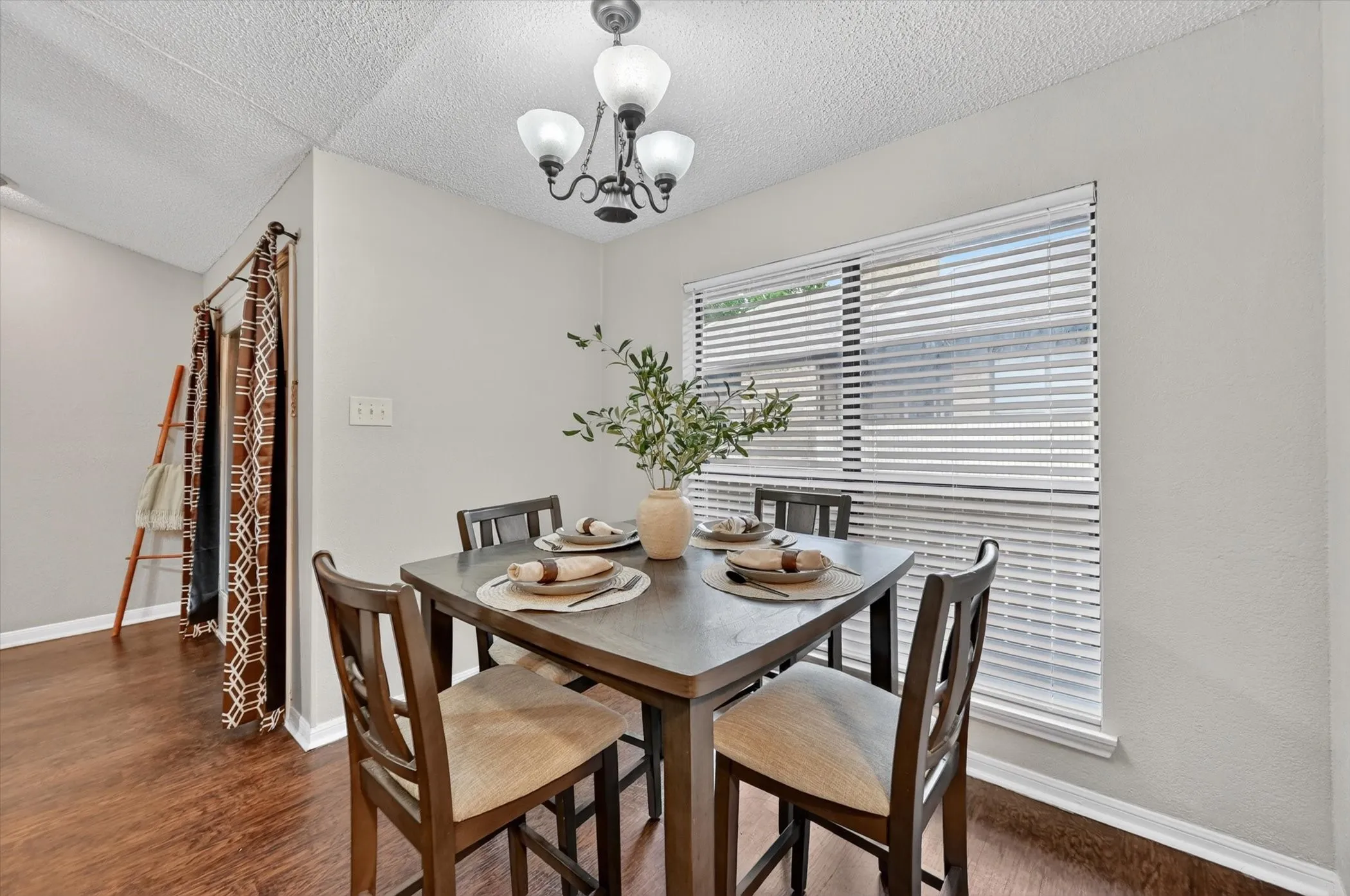 Dining area featuring wood-finish flooring, a window with horizontal blinds, and a multi-light ceiling fixture