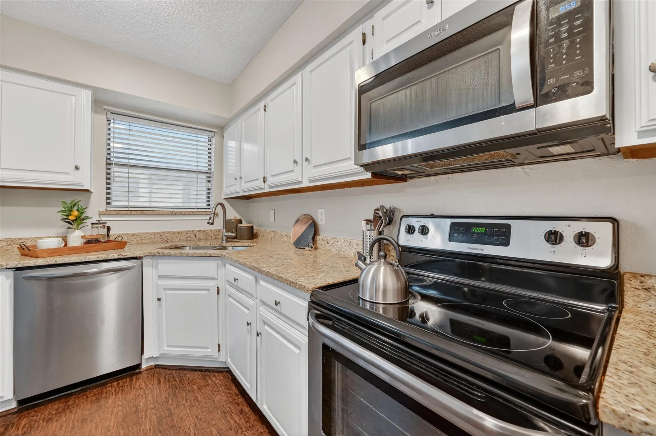 Kitchen featuring white cabinetry, light-toned granite countertops, stainless steel appliances including a built-in microwave and dishwasher, and wood-finish flooring