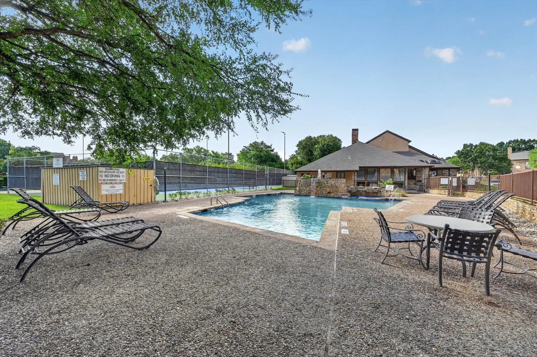 Outdoor swimming pool with a surrounding aggregate concrete deck, an integrated water feature, and a privacy fence