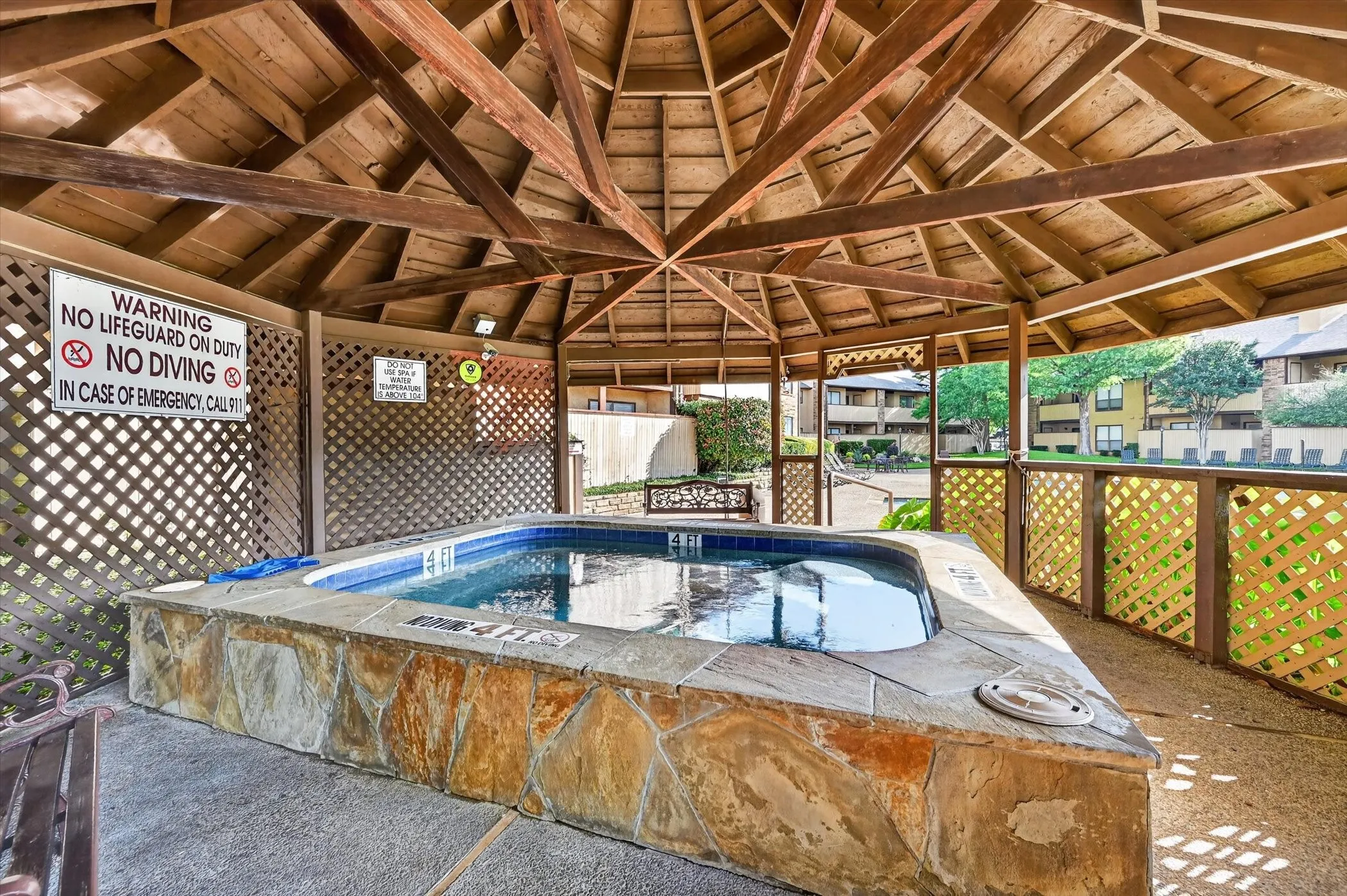 Shaded spa featuring a natural stone surround and blue tile interior