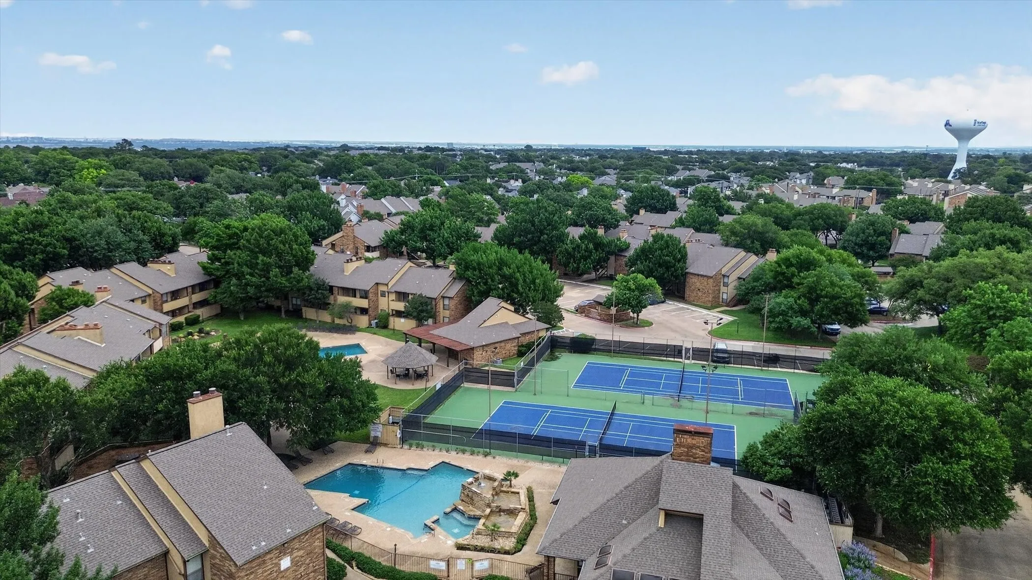 Aerial perspective showcasing multiple residential buildings, two swimming pools, two tennis courts, and mature landscaping