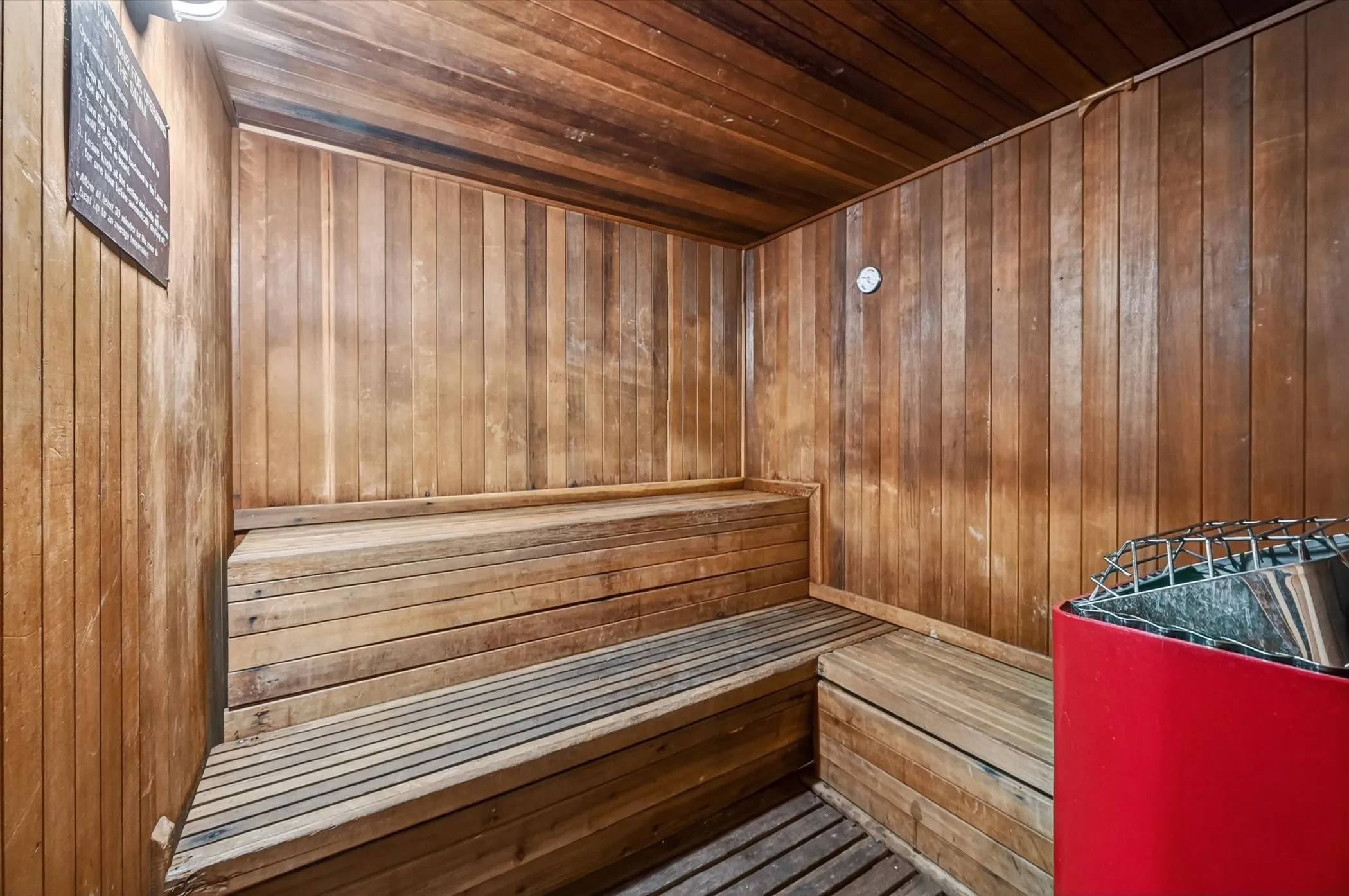 Wood-paneled sauna featuring tiered wooden benches and a red-finished sauna heater