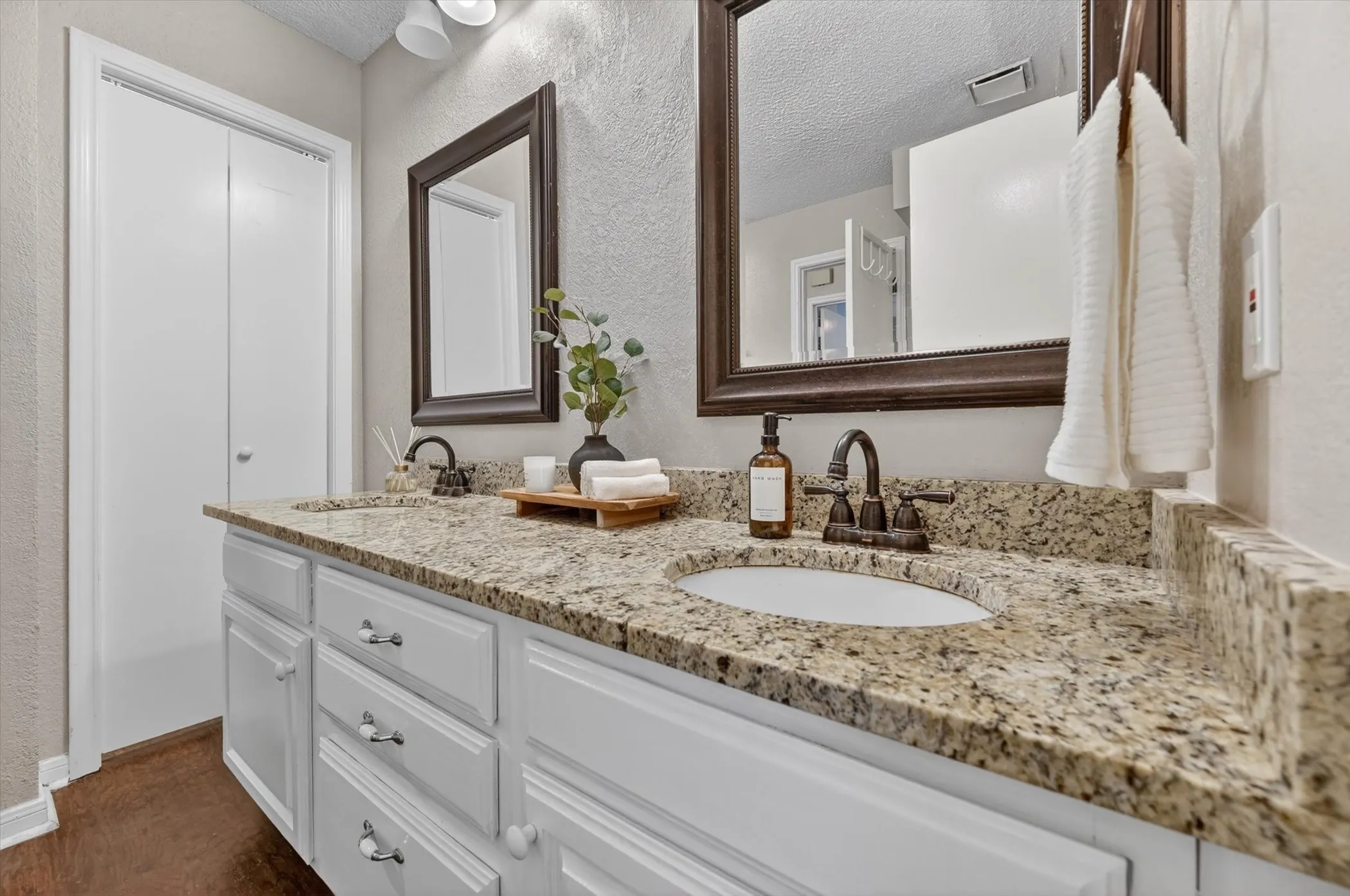 Bathroom vanity featuring dual undermount sinks with bronze-finish faucets, a granite countertop, white cabinetry with decorative hardware, and two framed mirrors