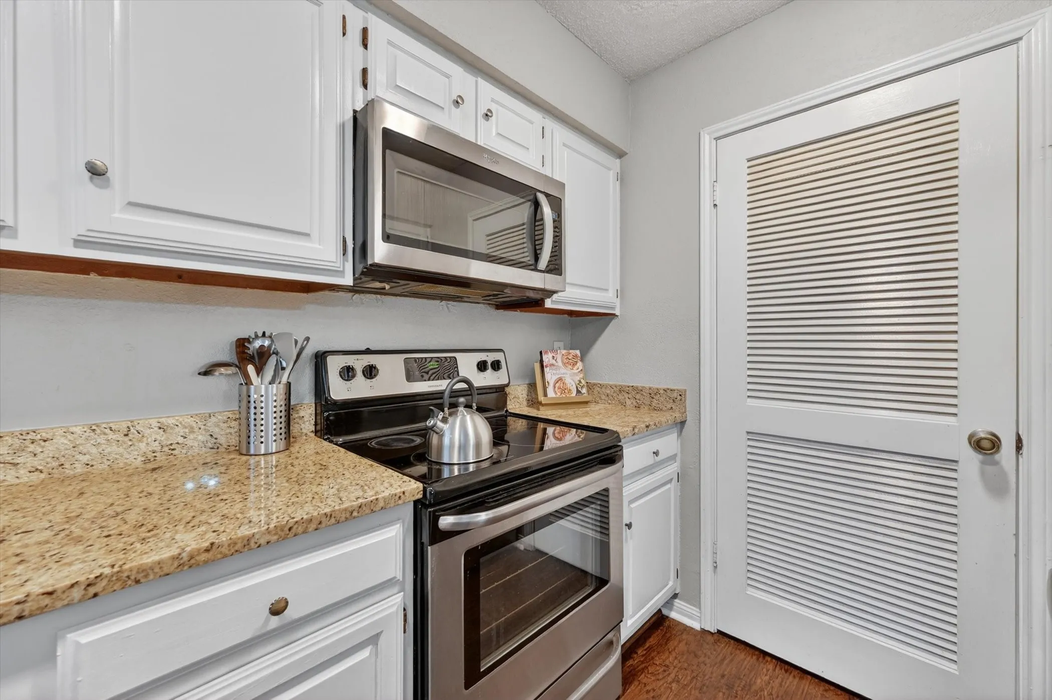 Kitchen featuring granite countertops, stainless steel appliances, white cabinetry, and wood-finish flooring