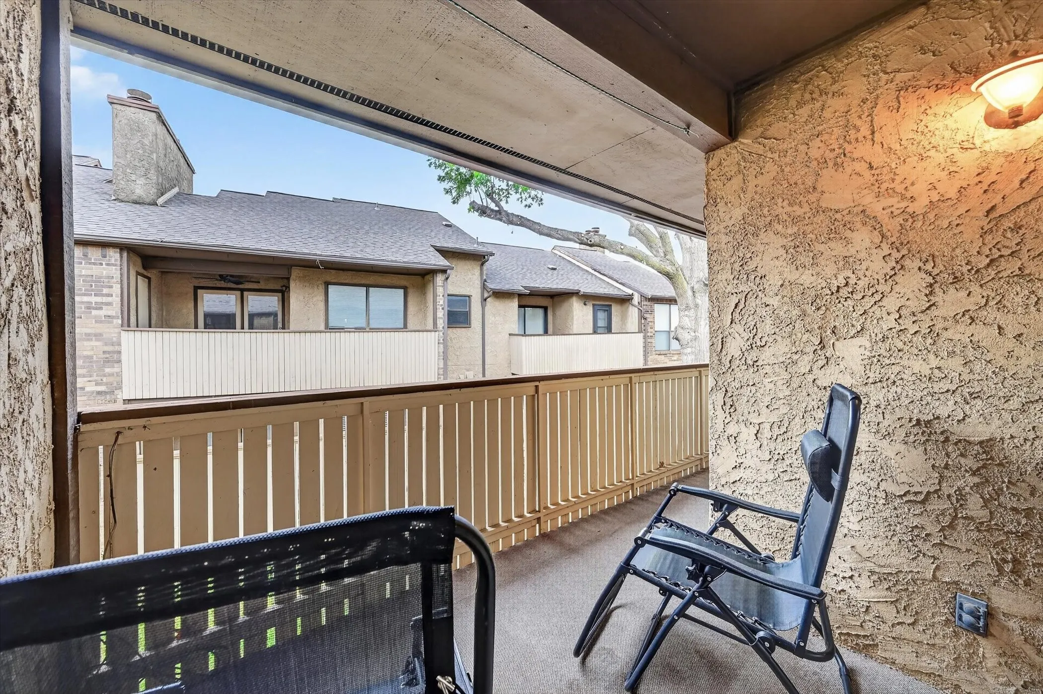 Private balcony featuring textured stucco siding, a protective overhead covering, and an exterior wall-mounted light fixture