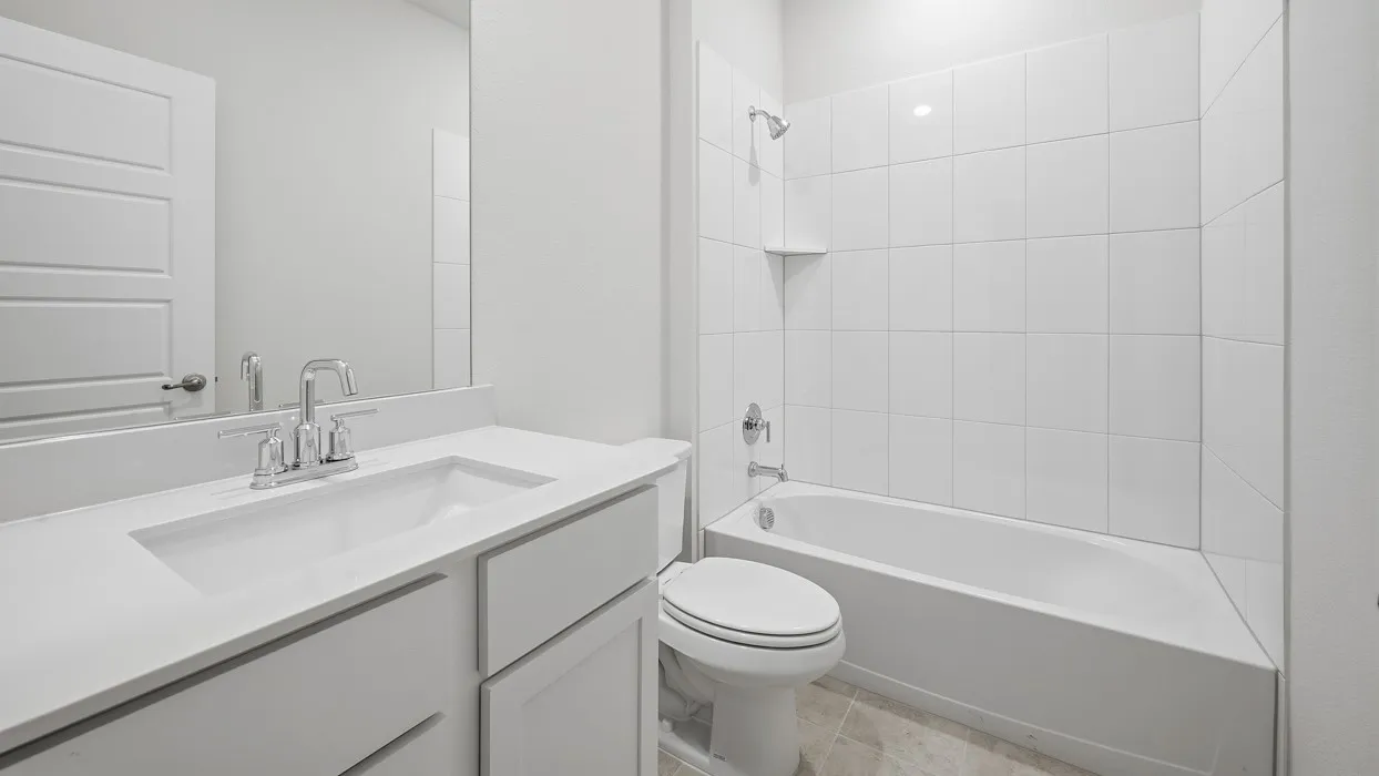 Bathroom featuring a white vanity with an integrated sink, polished chrome faucet, a large wall mirror, and a white tiled shower-tub combination with a chrome shower head and fixtures