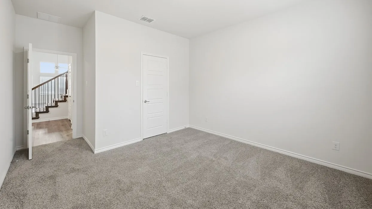 Carpeted room with white walls, a modern white door with horizontal paneling, and an open doorway revealing a wood-finish staircase with dark banisters