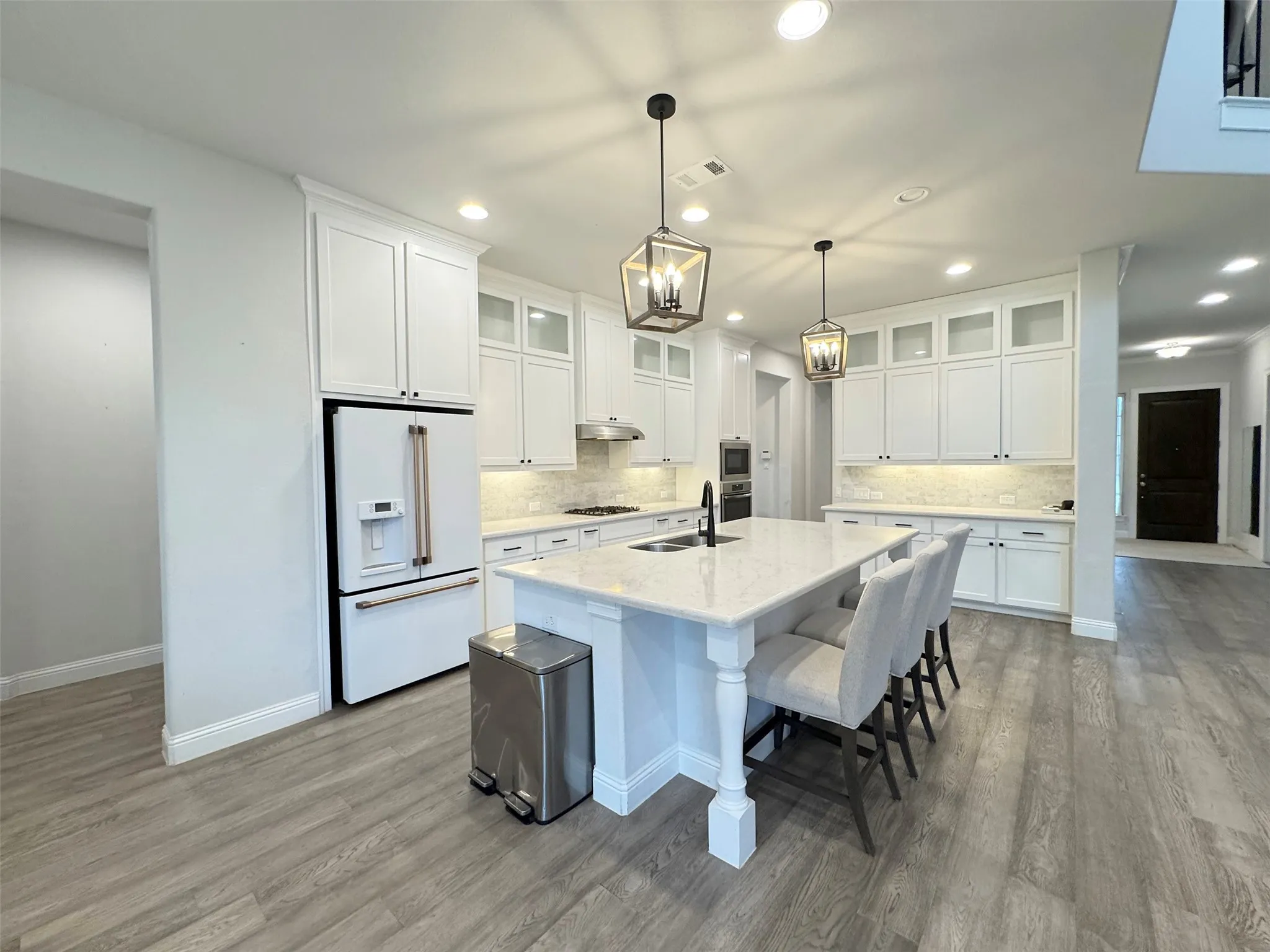 Modern kitchen featuring an expansive central island with seating, white shaker-style cabinetry, stainless steel appliances, and wood-finish flooring