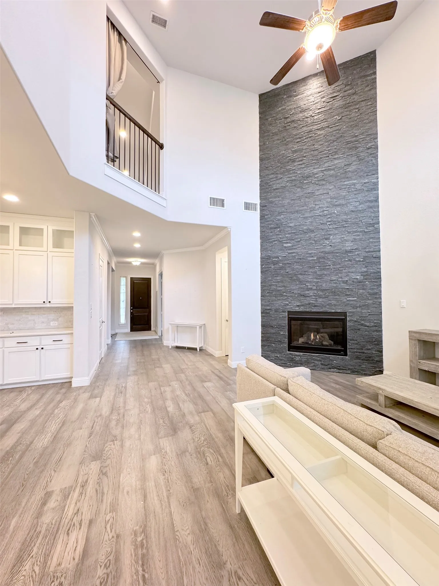 Spacious open-concept living area featuring a floor-to-ceiling stacked stone fireplace, vaulted ceiling with a ceiling fan, and wood-finish flooring
