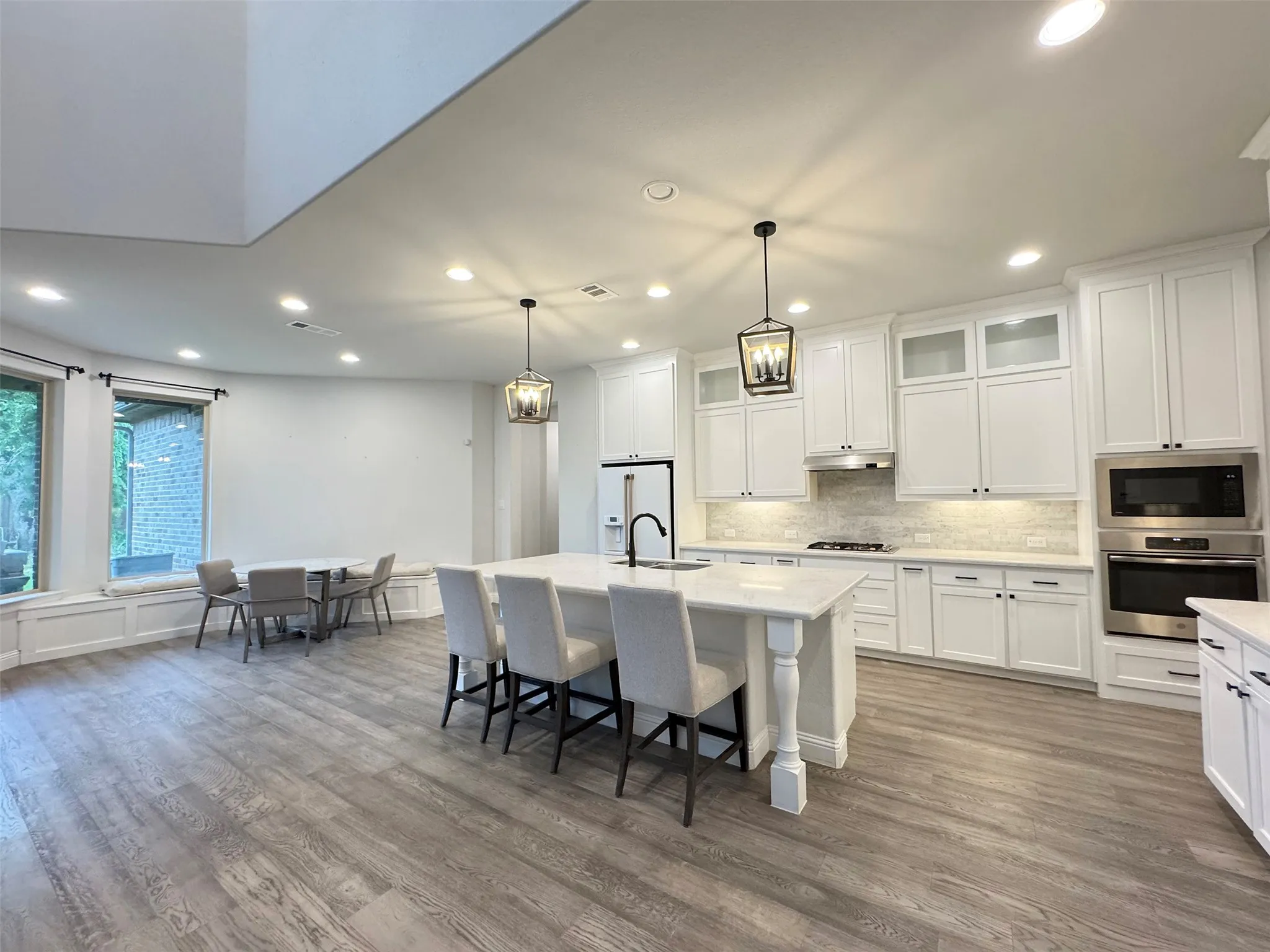 Kitchen featuring white cabinetry, stainless steel appliances, a center island with pendant lighting, and wood-finish flooring