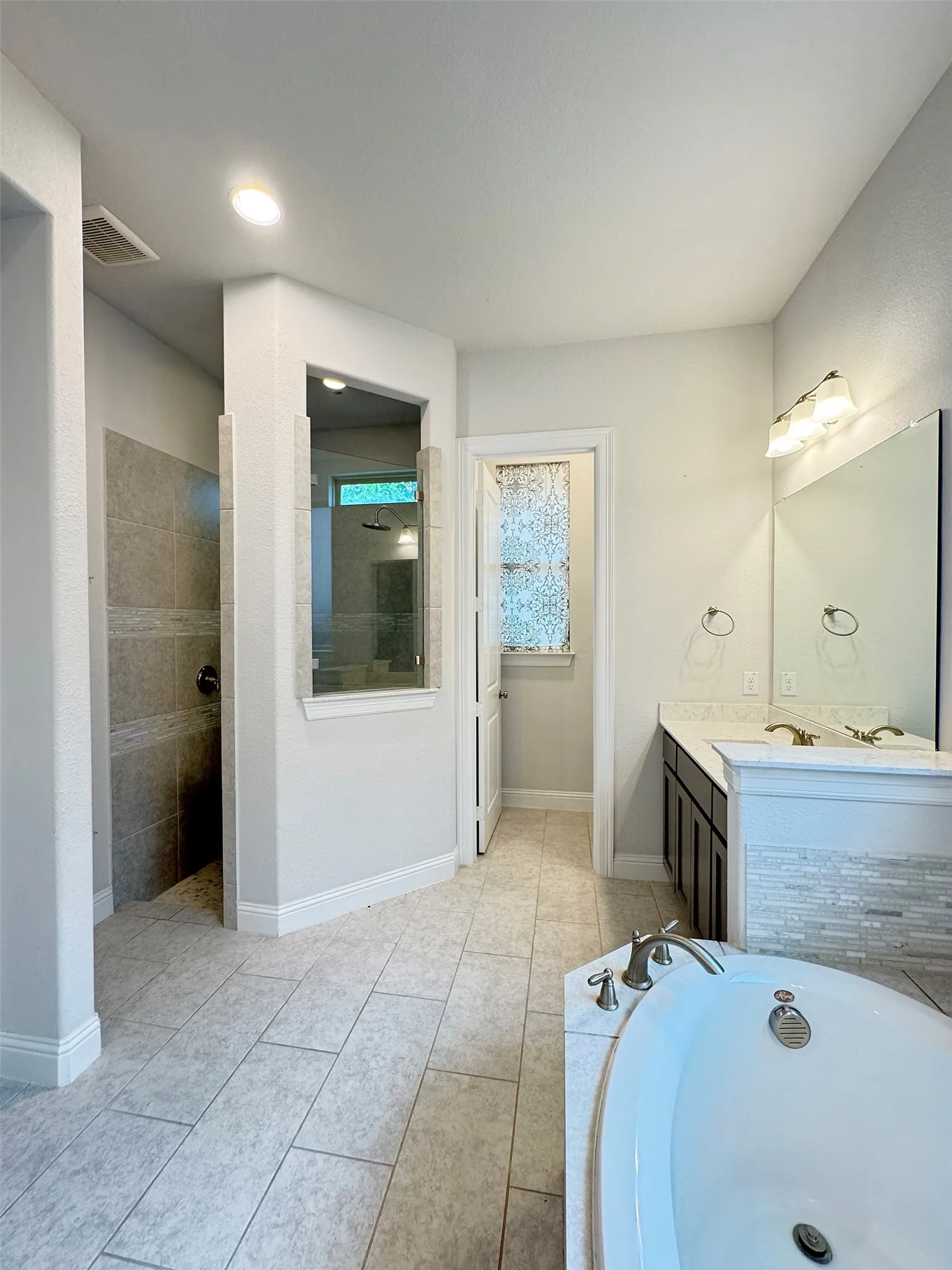 Spacious bathroom featuring a built-in soaking tub with deck-mounted fixtures, a dual vanity with undermount sinks and individual mirrors, and a walk-in shower with tiled walls