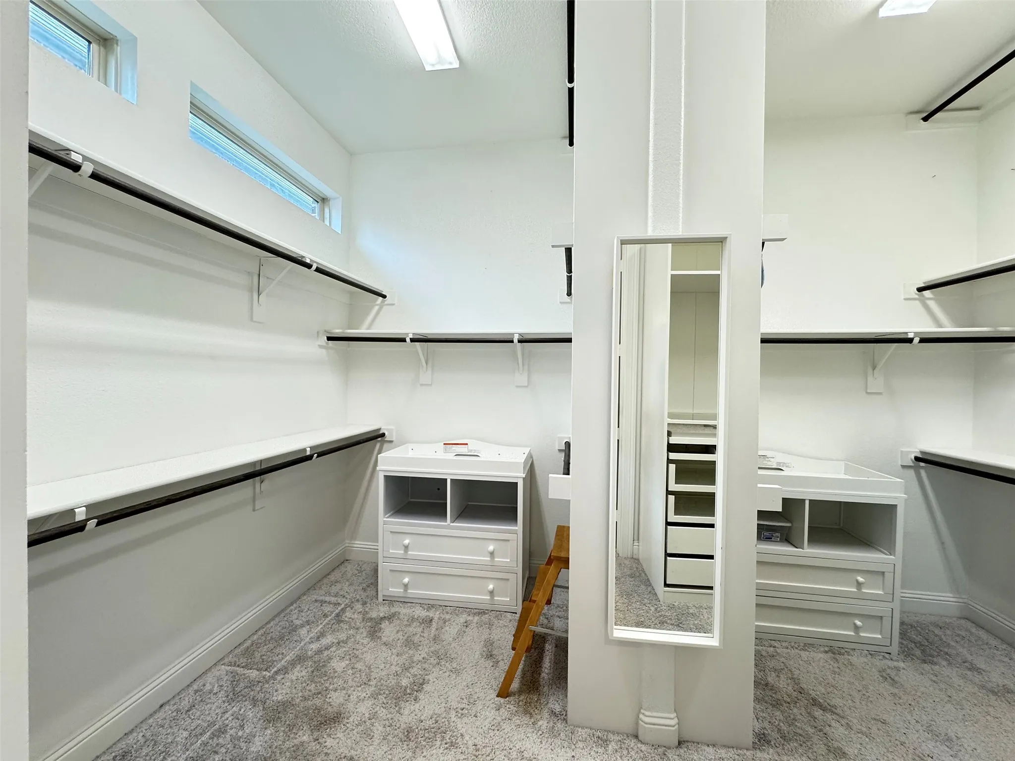 Spacious walk-in wardrobe featuring multiple shelving units, hanging rods, two built-in drawer cabinets, a full-length mirror, and upper transom windows