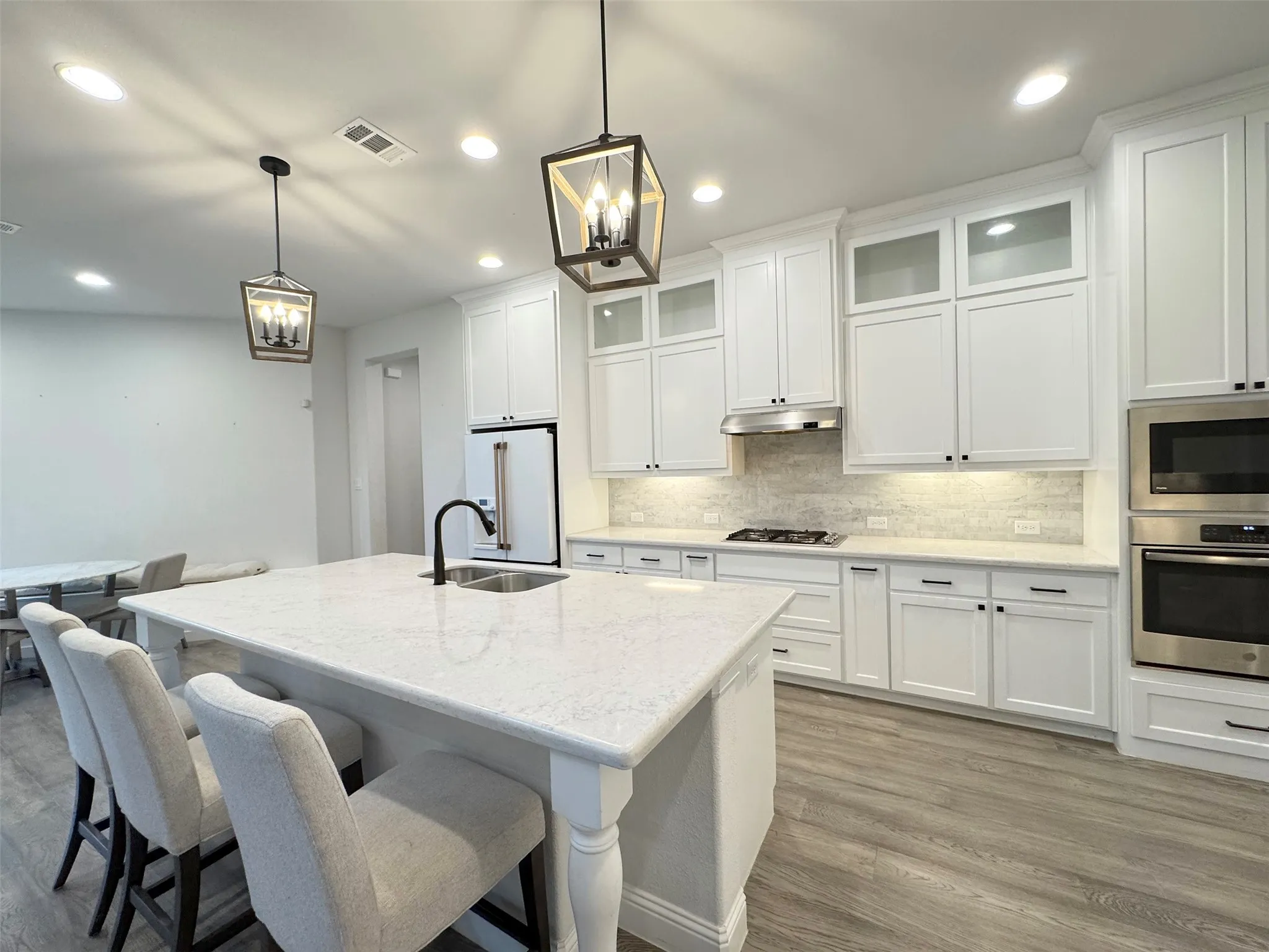 Gourmet kitchen featuring a large central island with an integrated sink, white shaker cabinetry, stainless steel appliances, and wood-finish flooring
