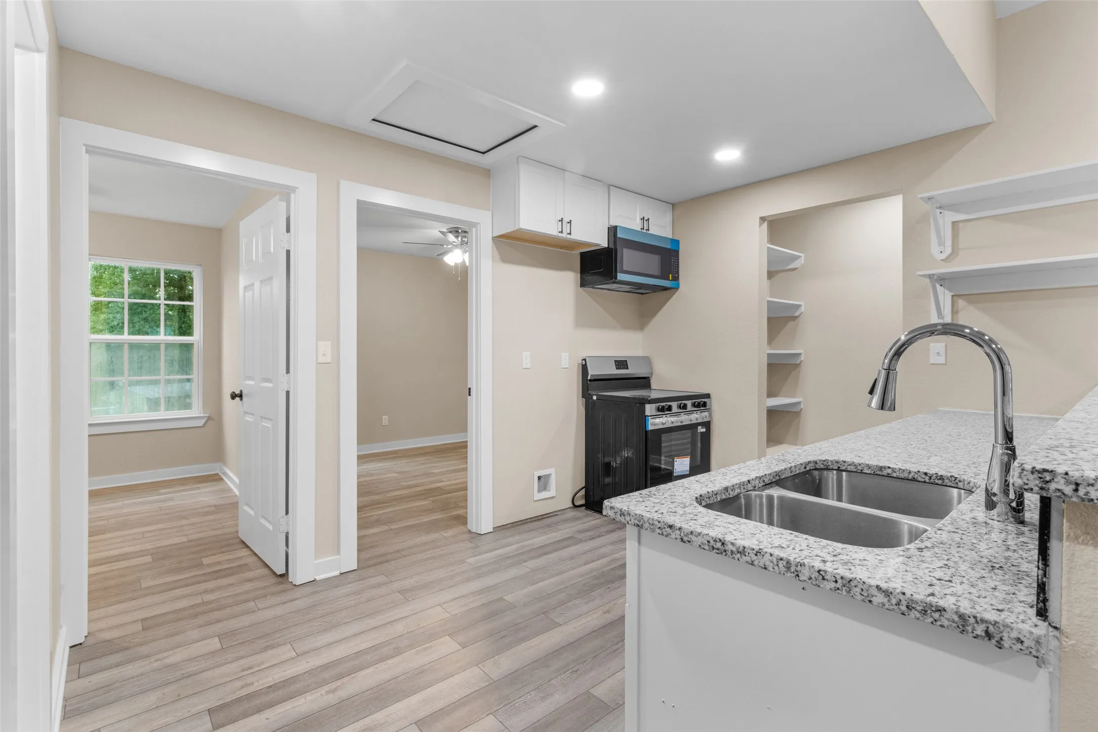Kitchen area featuring granite countertops, double basin stainless steel sink with gooseneck faucet, white cabinetry, and wood-finish flooring