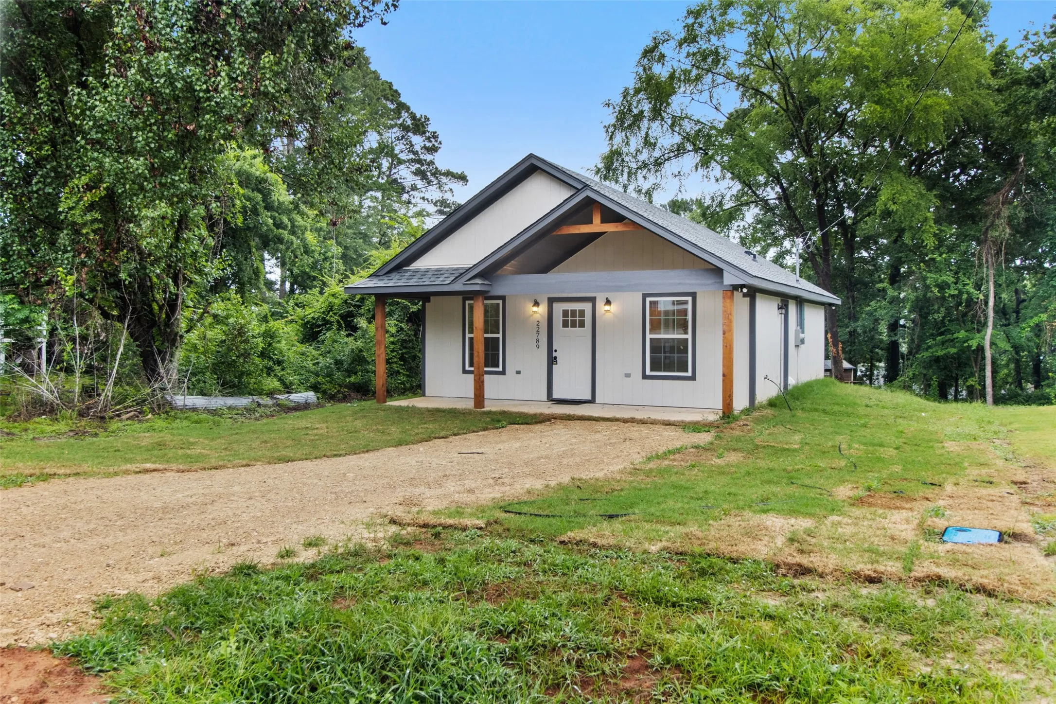 Contemporary single-story residence featuring a gravel driveway, covered front porch with exposed wooden posts, and a gabled roofline with dark trim