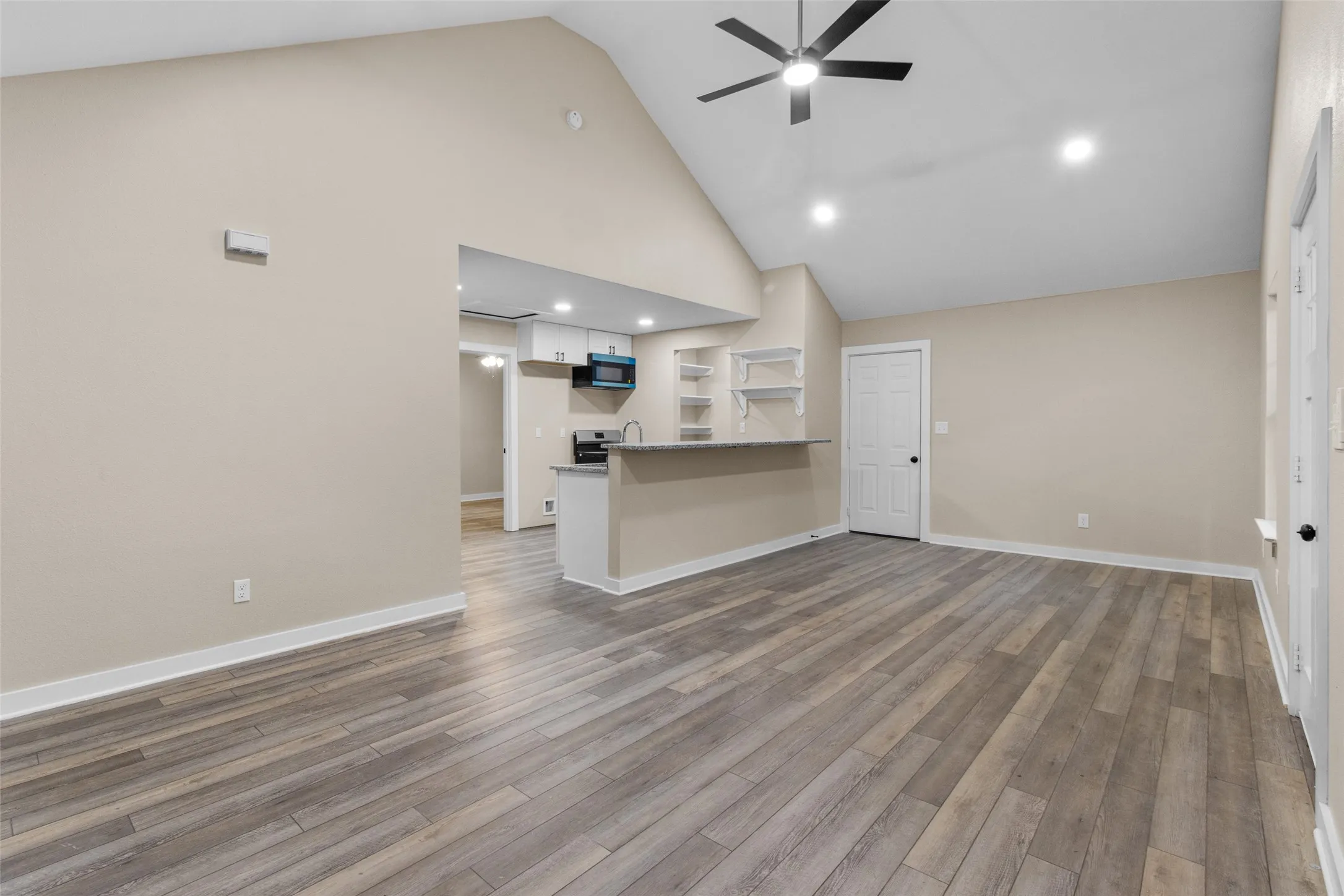 Spacious living area featuring wood-finish flooring and a vaulted ceiling with a ceiling fan