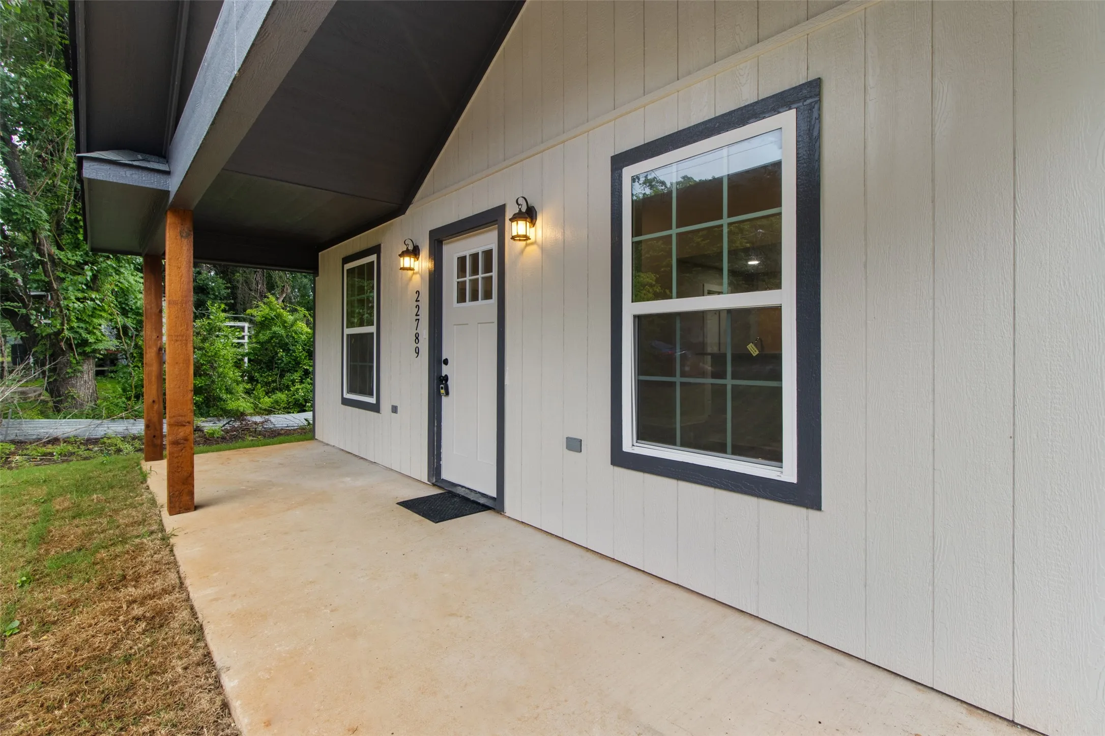 Exterior featuring vertical panel siding, a covered porch with exposed wood posts, and a solid entry door with upper window panes
