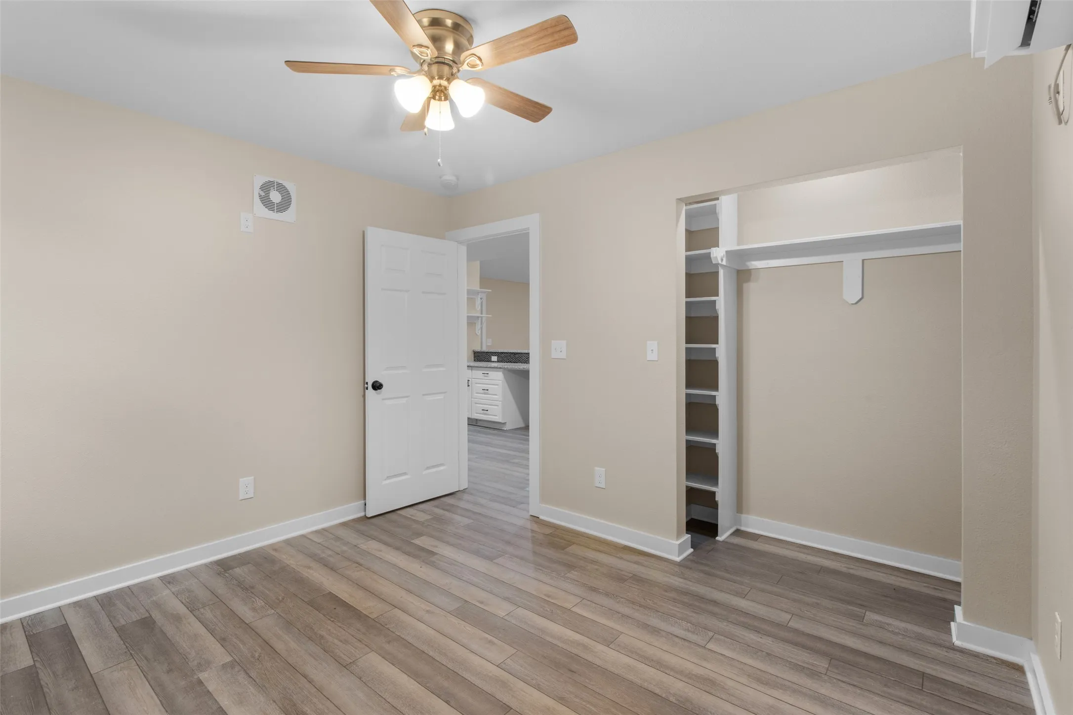 Interior room featuring wood-finish flooring, a ceiling fan with integrated lighting, and an open closet with shelving and a hanging rod