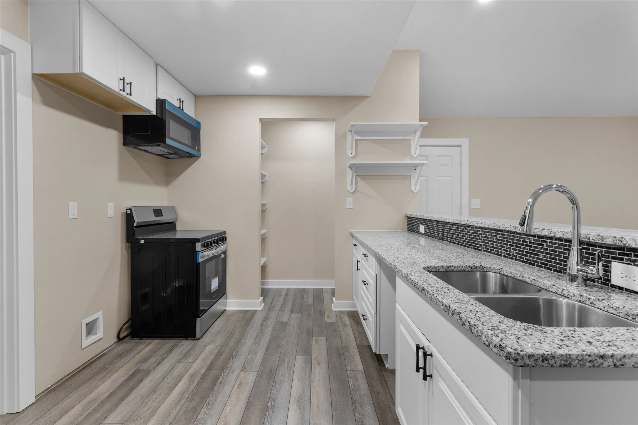 Kitchen featuring granite countertops, a double basin stainless steel sink with a high-arc faucet, and white cabinetry with dark hardware