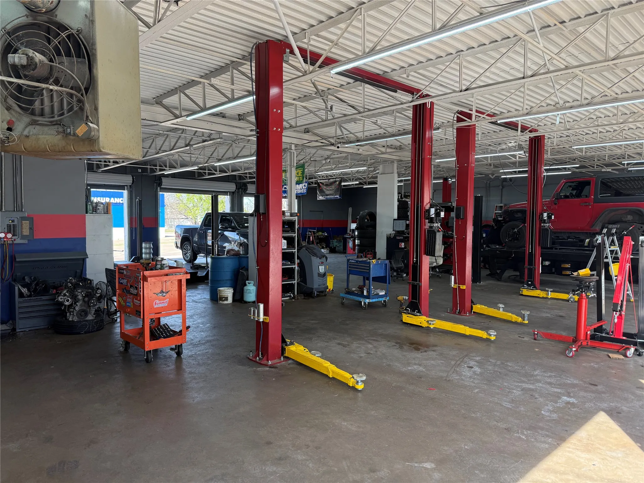 Spacious service bay featuring multiple vehicle lifts, overhead lighting, and an industrial-style ceiling with exposed trusses