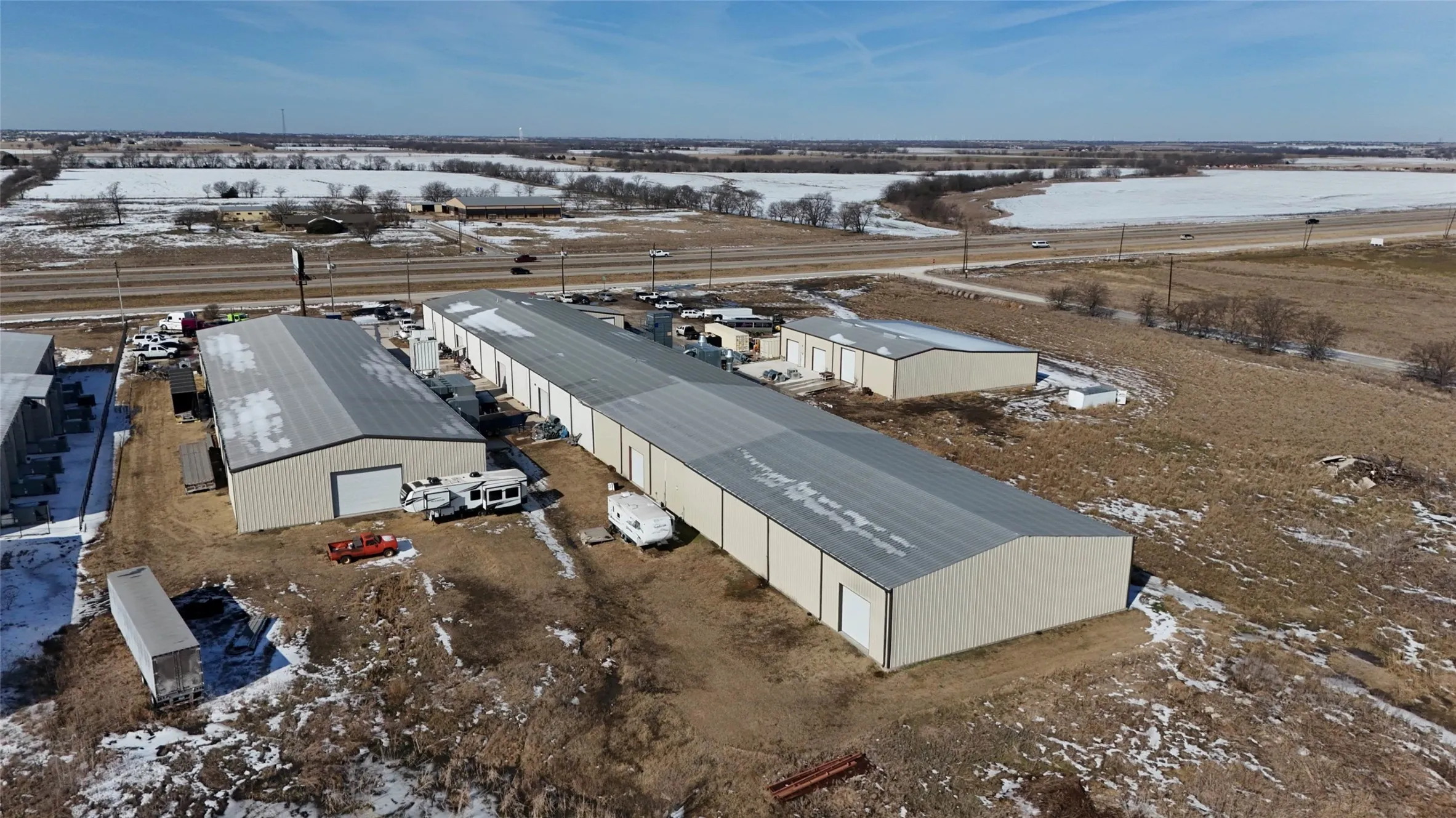 Industrial complex featuring multiple metal buildings with pitched roofs, individual roll-up doors, and ample exterior space