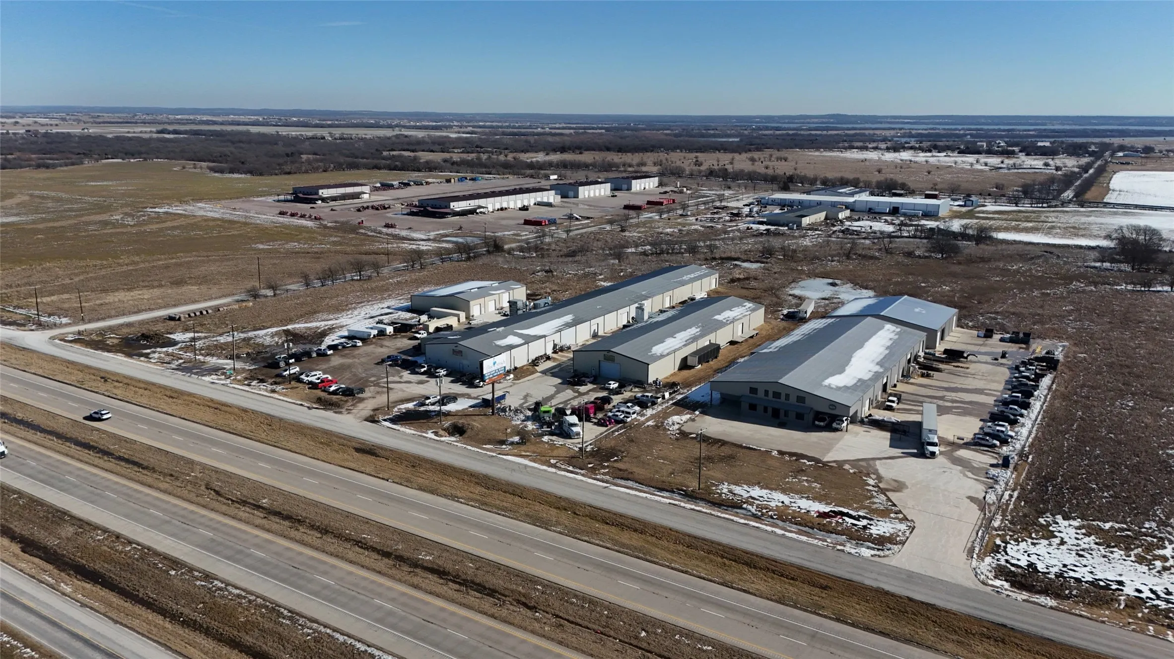 Industrial park featuring multiple buildings with metal siding and roofs, extensive asphalt paving, and I-35 highway frontage