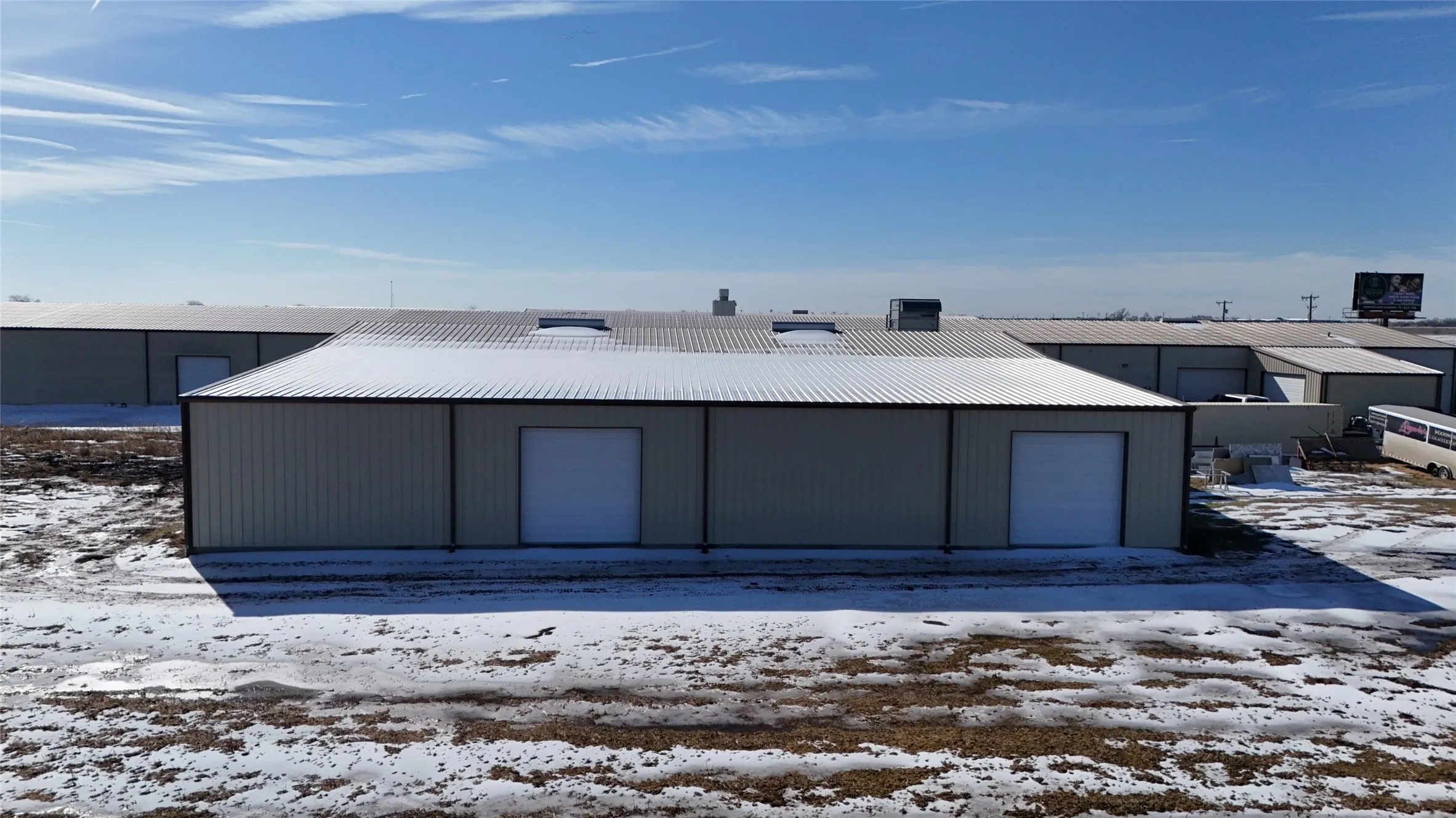 Industrial building featuring a metal roof, two roll-up garage doors, and multiple skylights