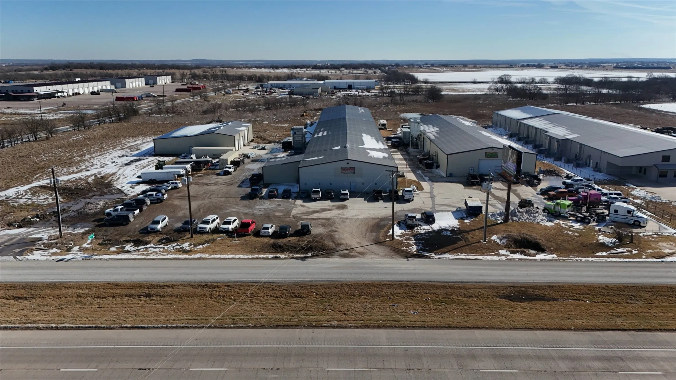 Expansive commercial property featuring multiple industrial buildings with metal siding and roofs, paved parking areas, and convenient roadway frontage