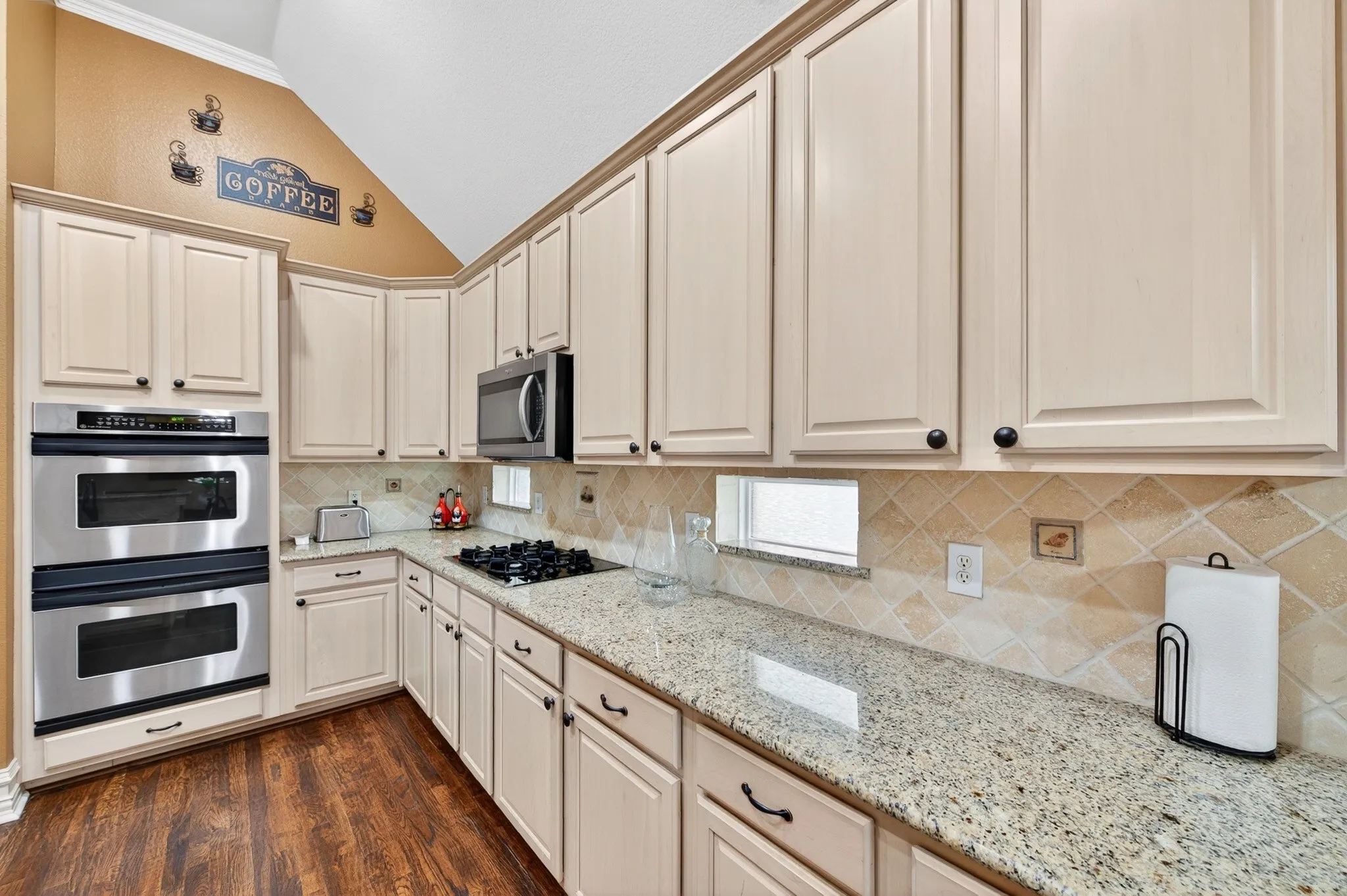 Kitchen featuring stainless steel double ovens, a gas cooktop, light-toned cabinetry with dark hardware, granite countertops, and wood-finish flooring