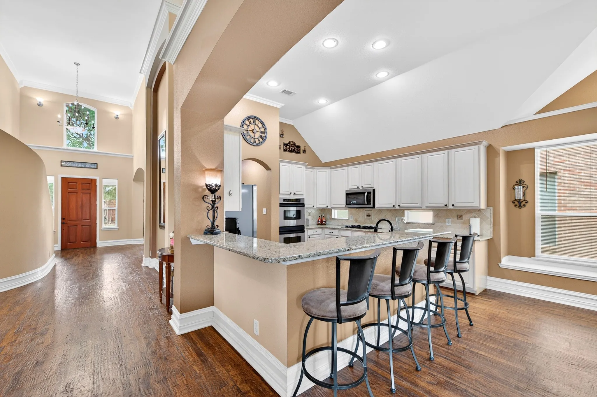 Open-concept kitchen featuring white cabinetry, integrated stainless steel appliances, and a breakfast bar with stone-finish countertops