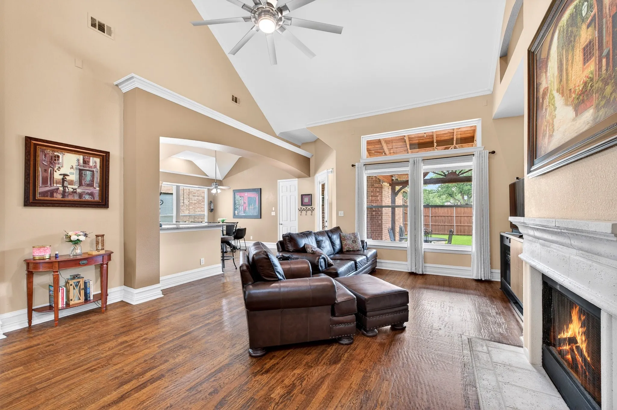 Spacious living area featuring high vaulted ceilings, elegant wood-finish flooring, and a decorative fireplace with a light-toned surround