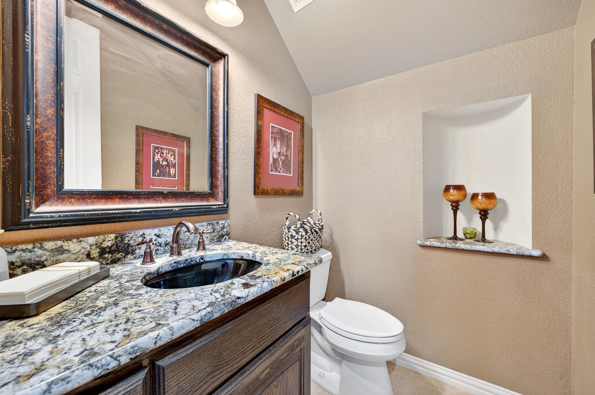 Bathroom featuring a granite countertop with an undermount sink and oil-rubbed bronze faucet, a framed mirror, a built-in wall niche with a stone shelf, and a white toilet