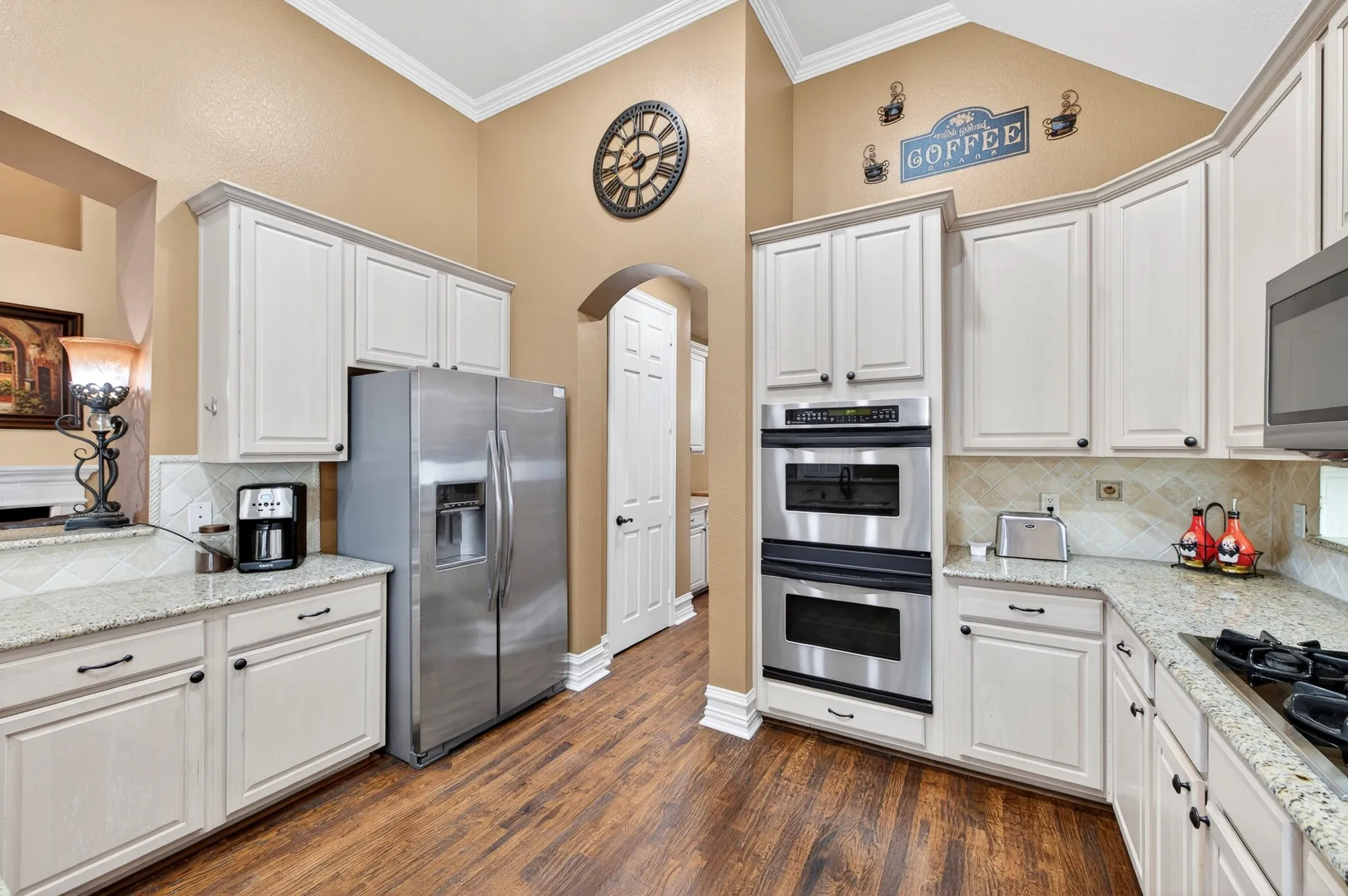 Kitchen featuring wood-finish flooring, white cabinetry, light-toned countertops, a stainless steel double oven, and a stainless steel refrigerator