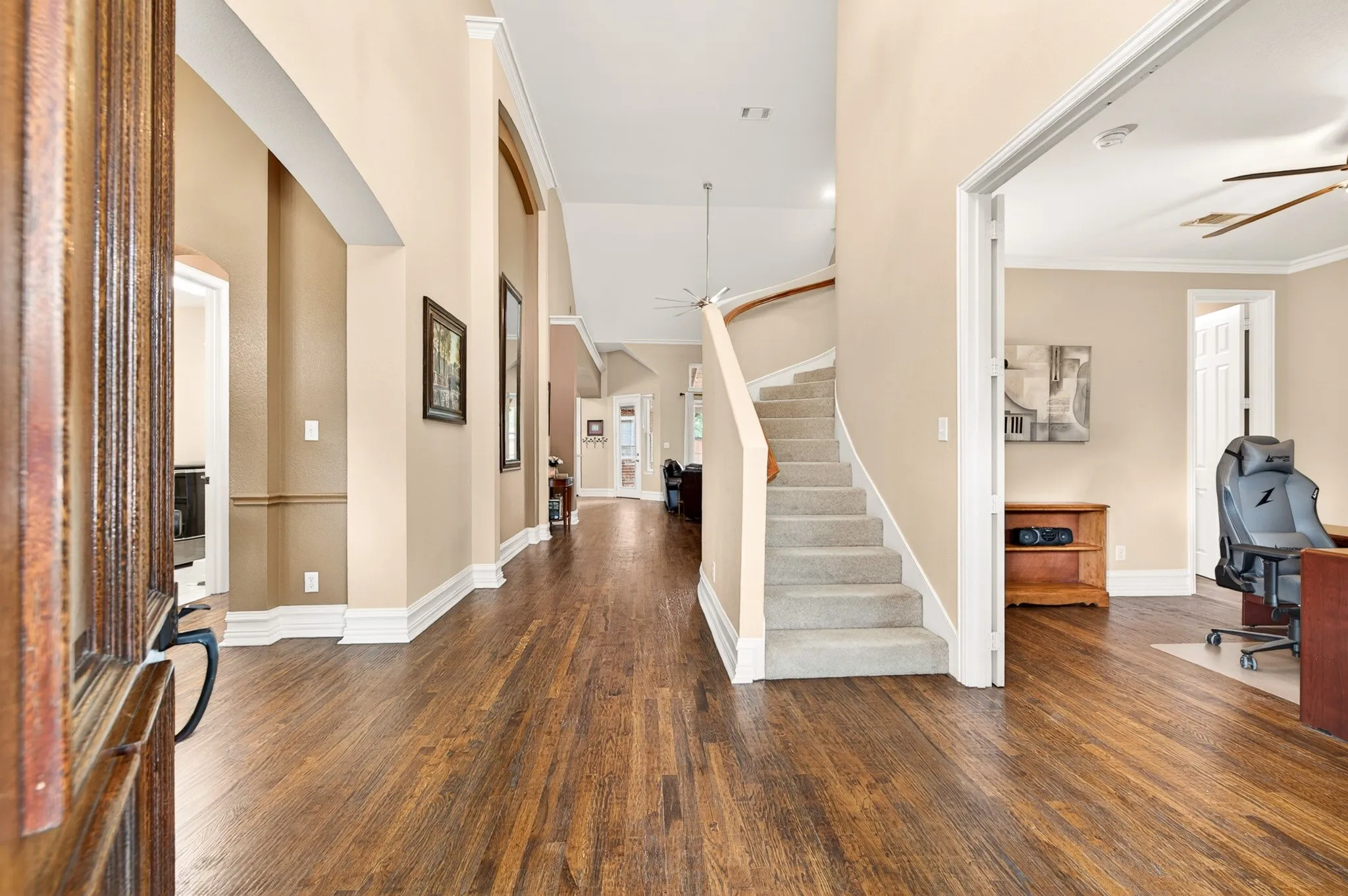 Spacious entryway featuring rich wood-finish flooring, a grand staircase with carpeted treads, tall ceilings and crown molding