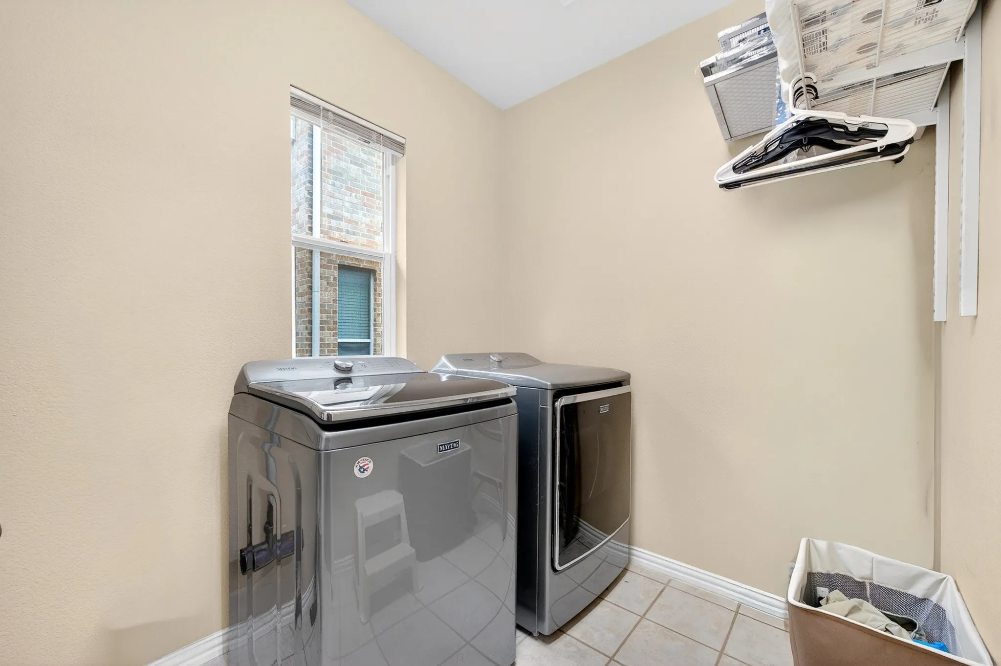 Dedicated laundry area featuring ceramic tile flooring, a window with blinds, and light-toned wall finishes