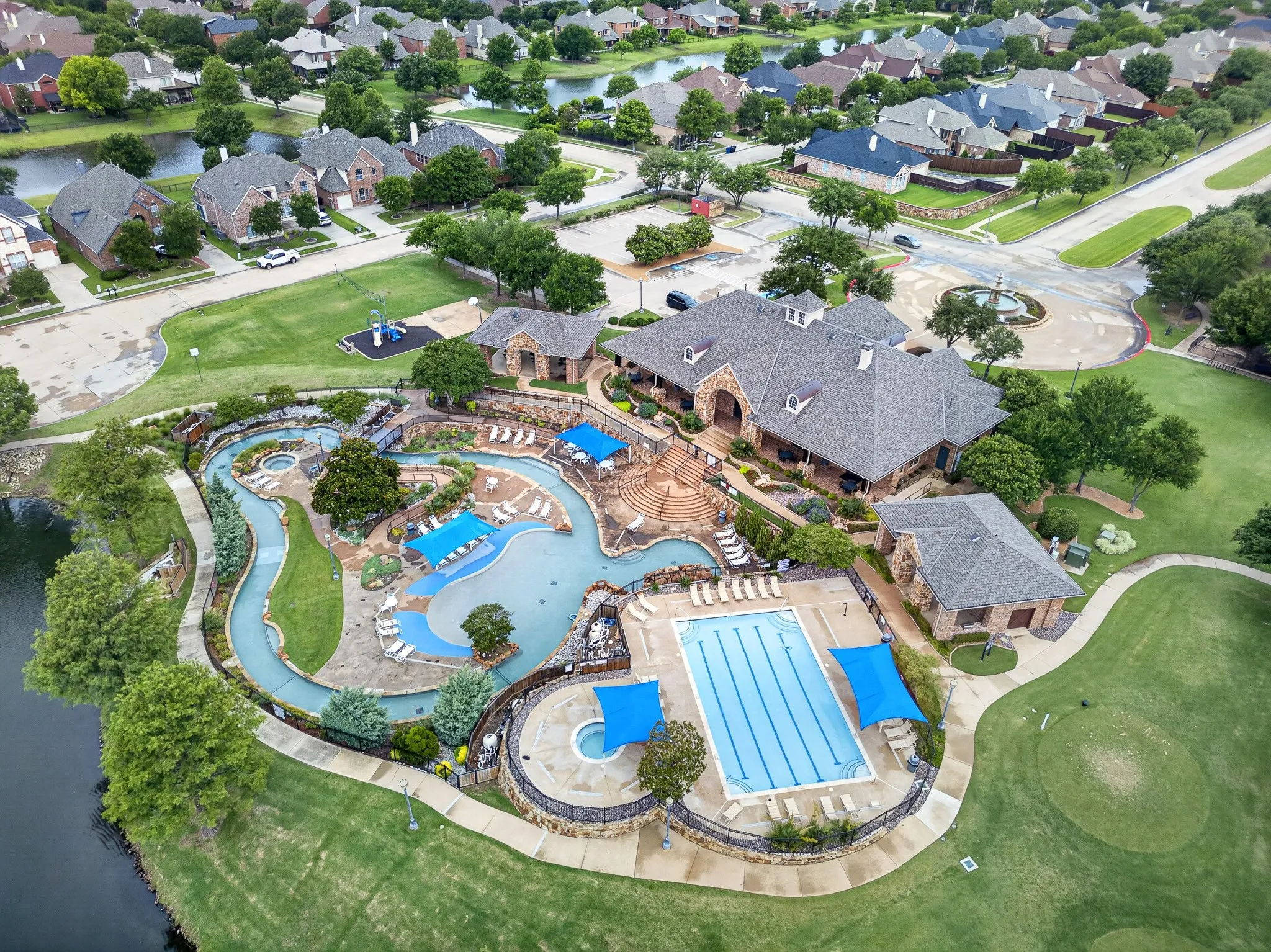 Expansive community amenity center featuring a leisure pool with a lazy river, a lap pool, a children's play structure, and a clubhouse building with a stone exterior