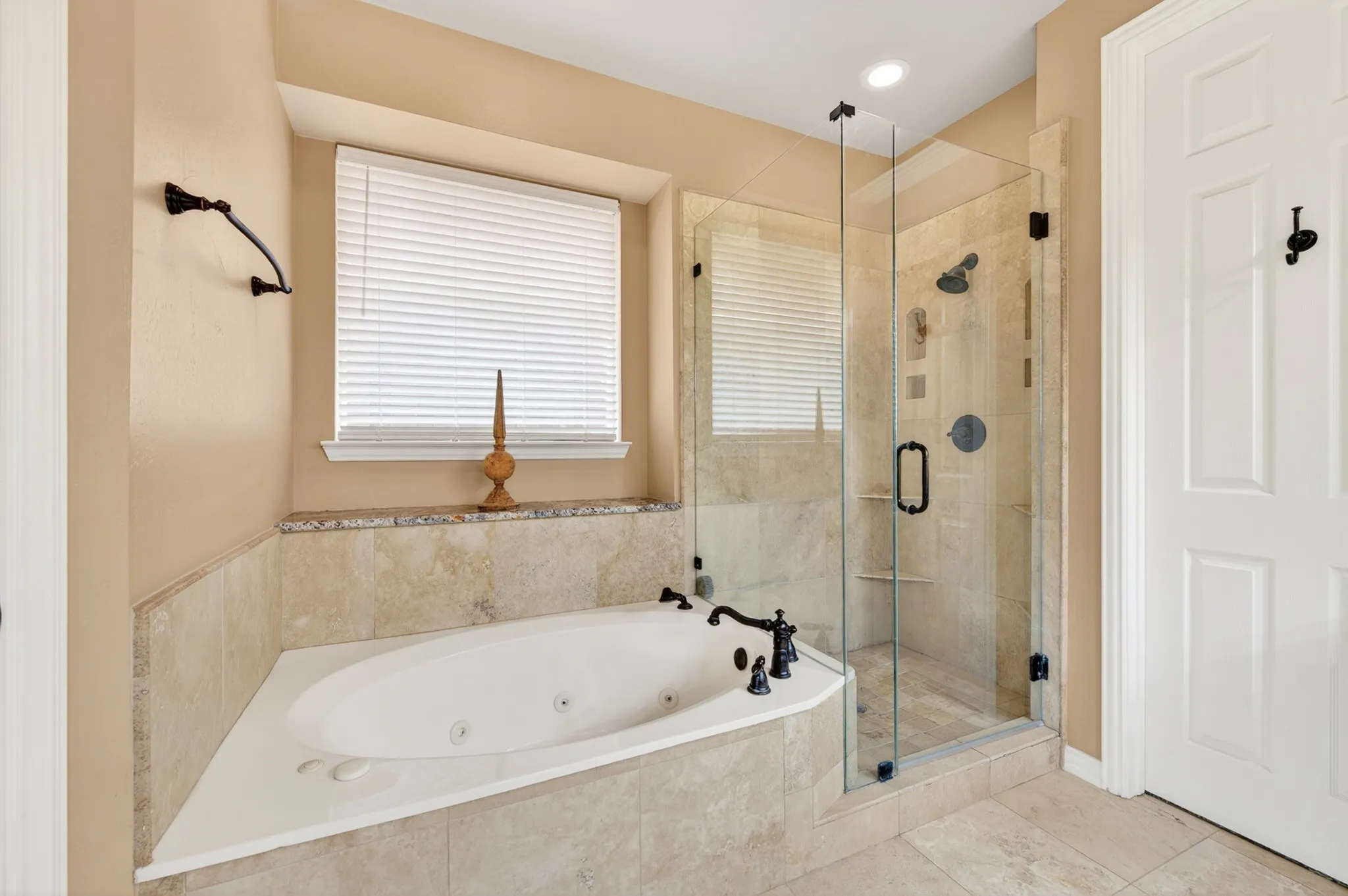 Corner soaking tub with dark bronze fixtures, framed by a tiled surround with a granite countertop