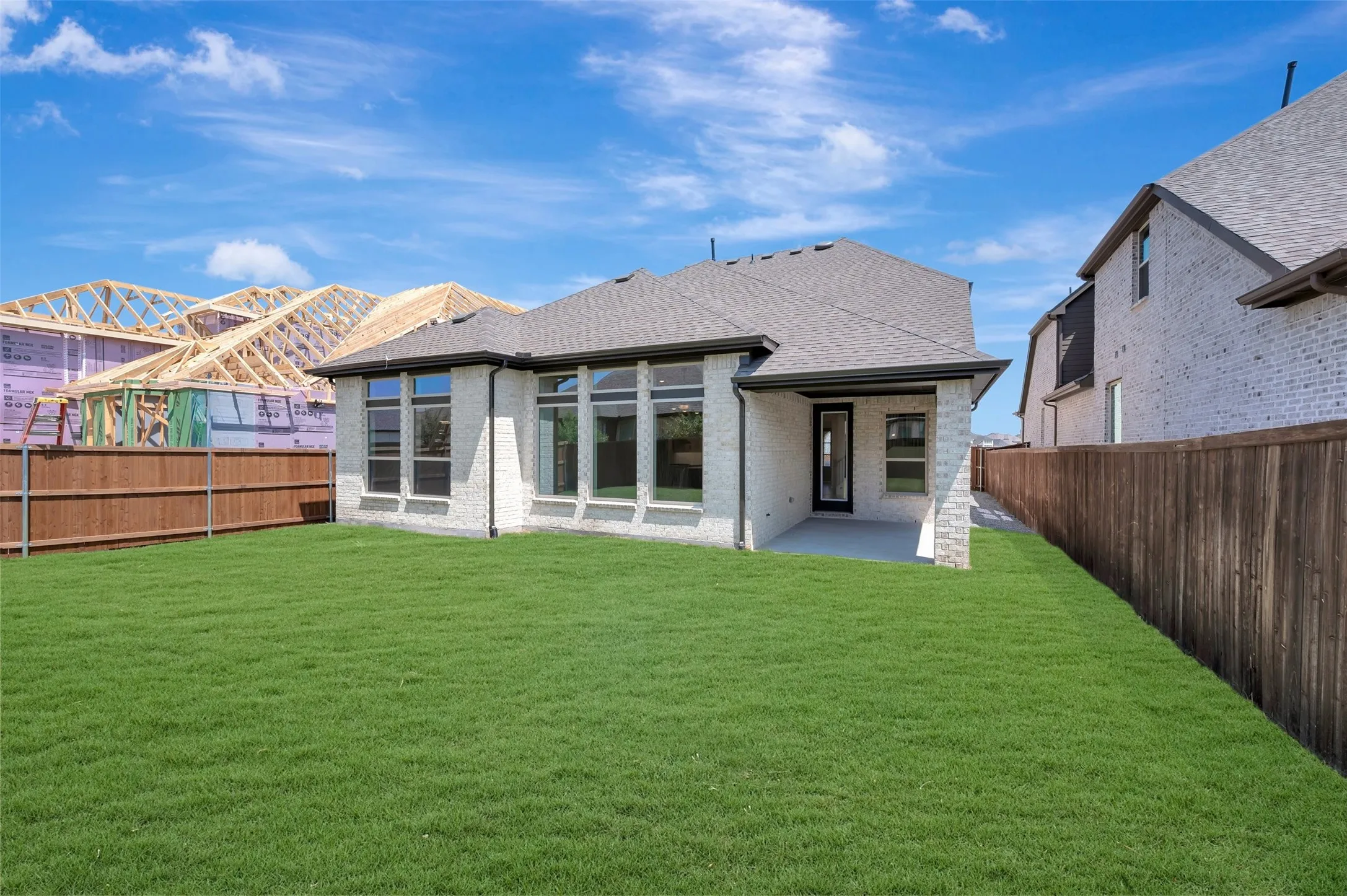 Expansive backyard featuring a manicured lawn, wood fencing, and a covered concrete patio