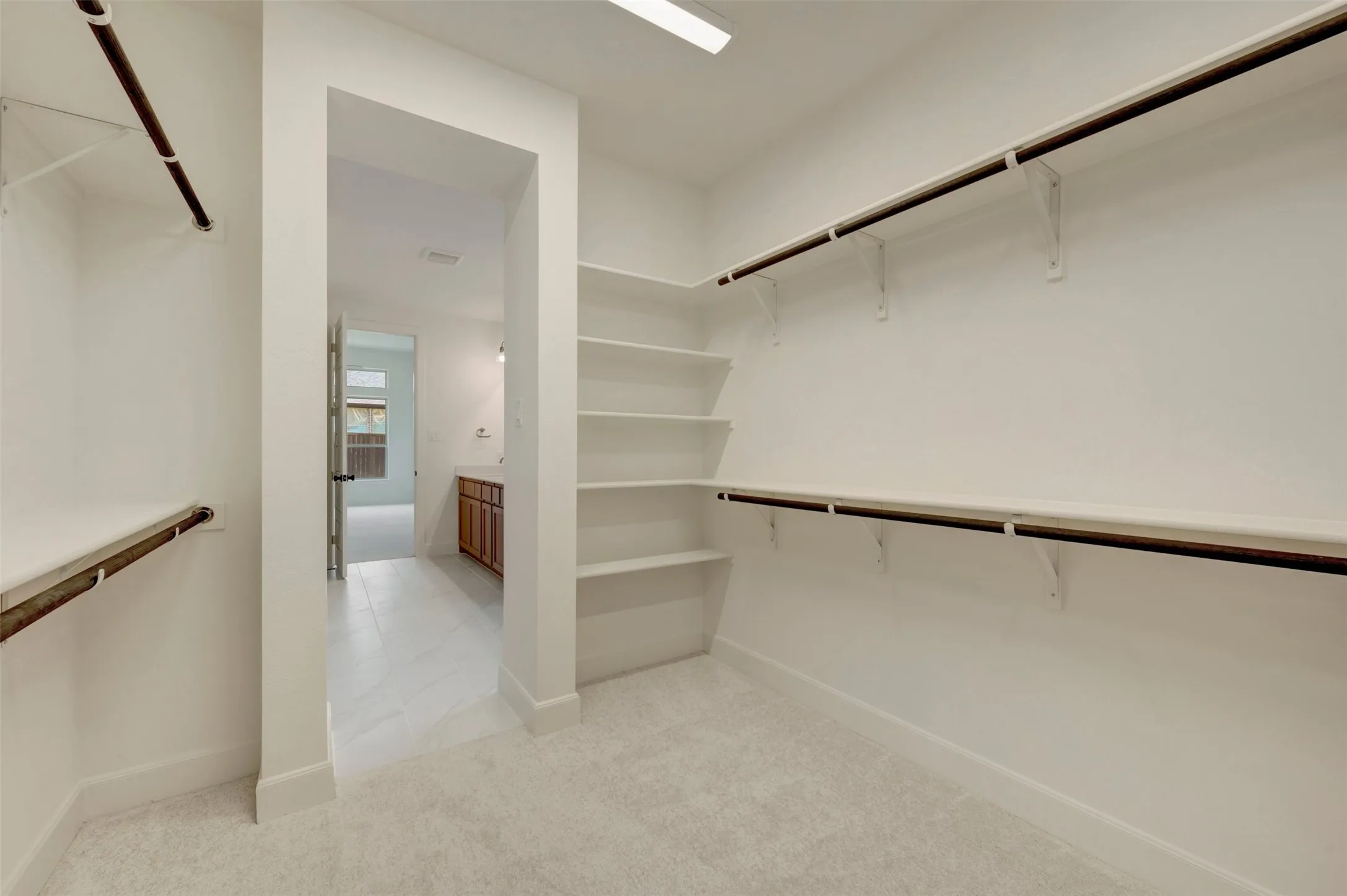 Spacious walk-in closet featuring dual clothing rods with integrated hardware, abundant shelving, polished concrete flooring, and recessed lighting throughout