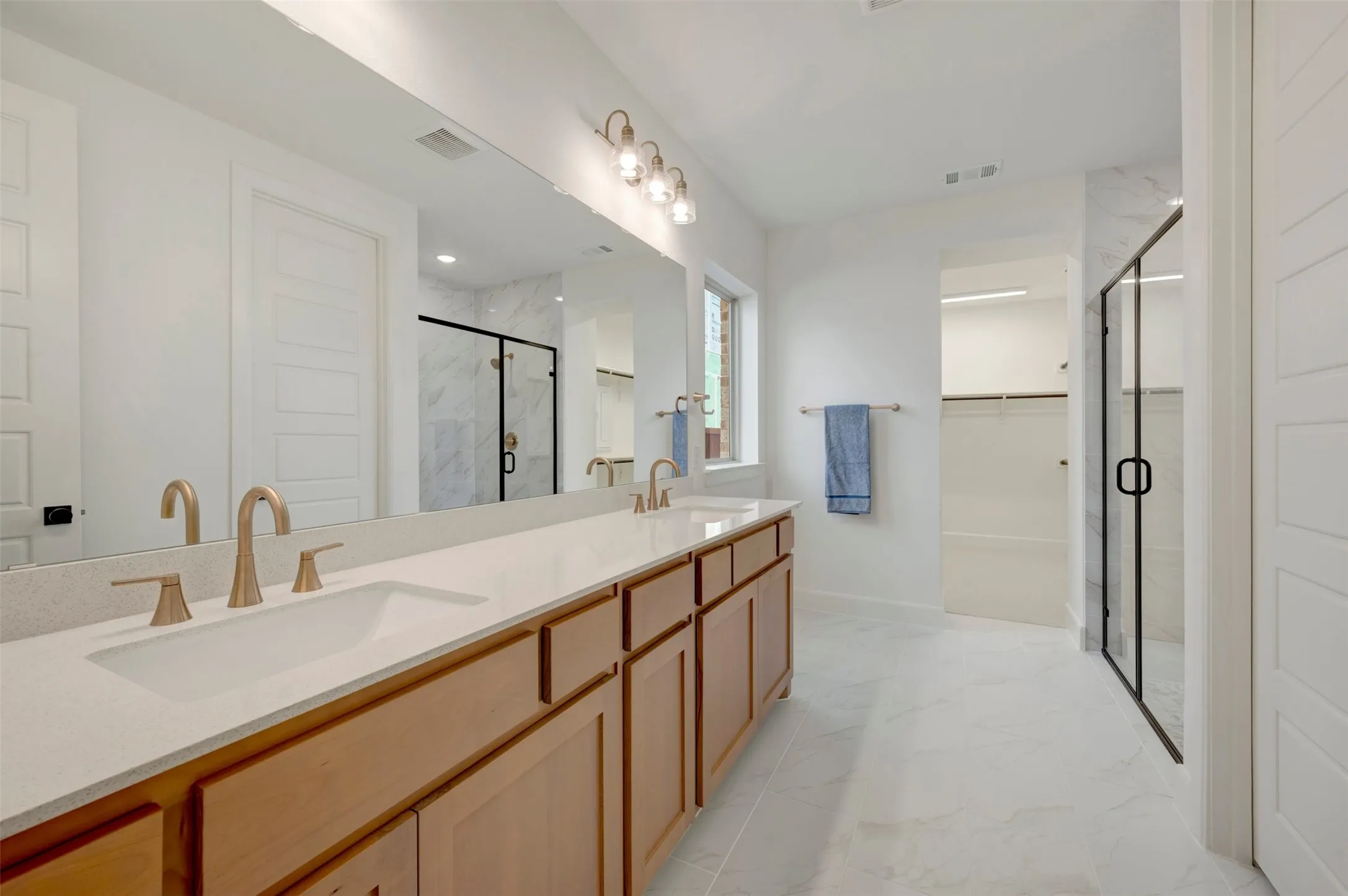 Dual vanity with stone-finish countertop, wood-finish cabinetry, and gold-tone fixtures